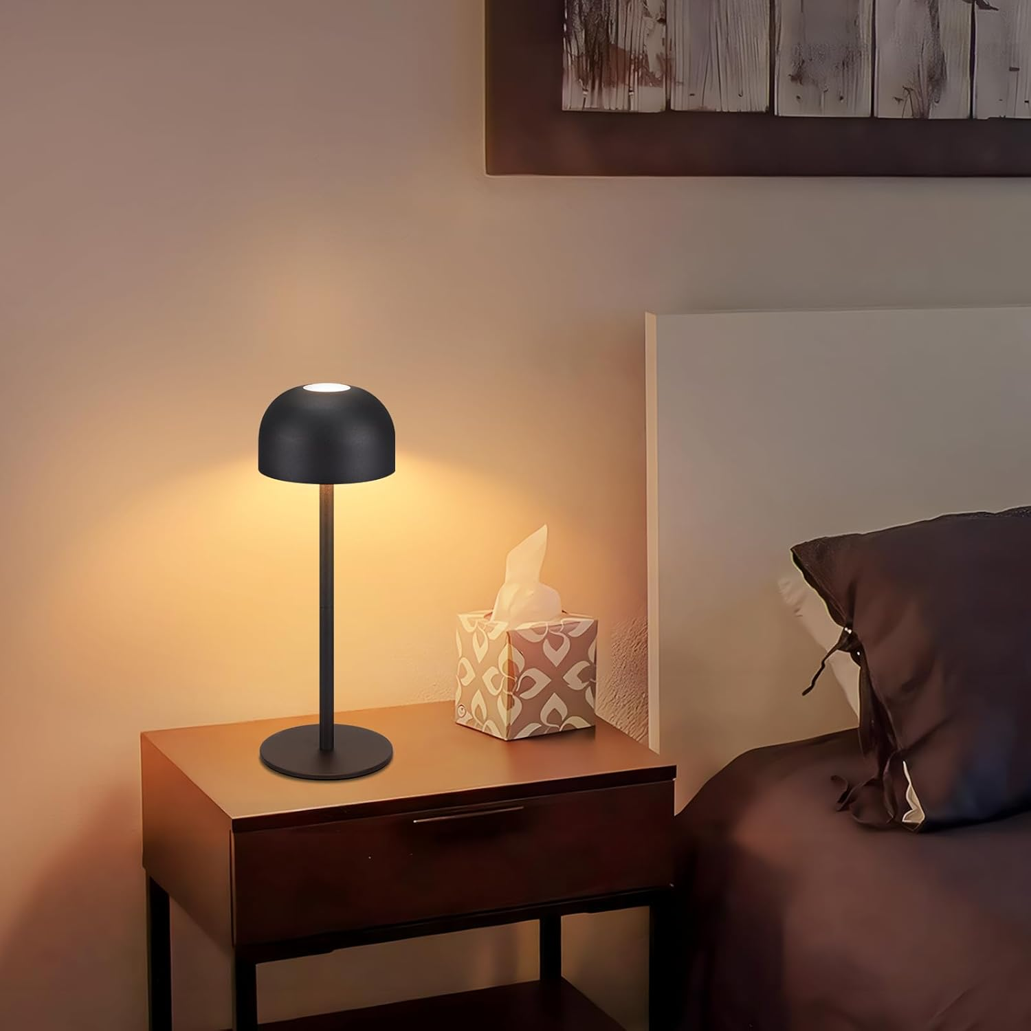 Czarna lampa stołowa w kształcie kopuły stoi na drewnianej szafce nocnej obok łóżka. Lampa jest zapalona.