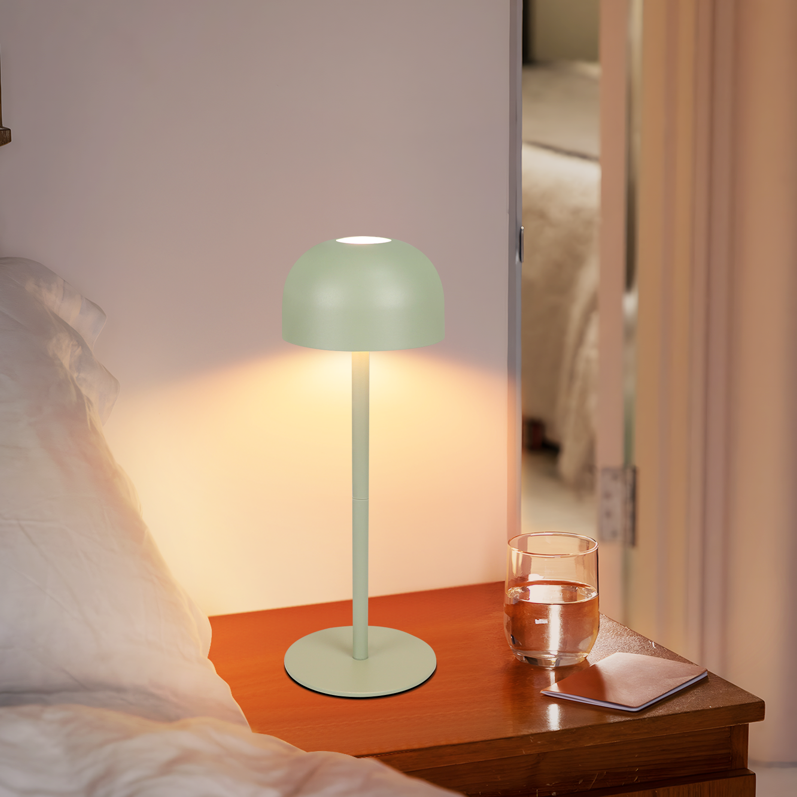 Zielona lampa stołowa z kloszem w kształcie kopuły na stoliku nocnym, ze szklanką wody.