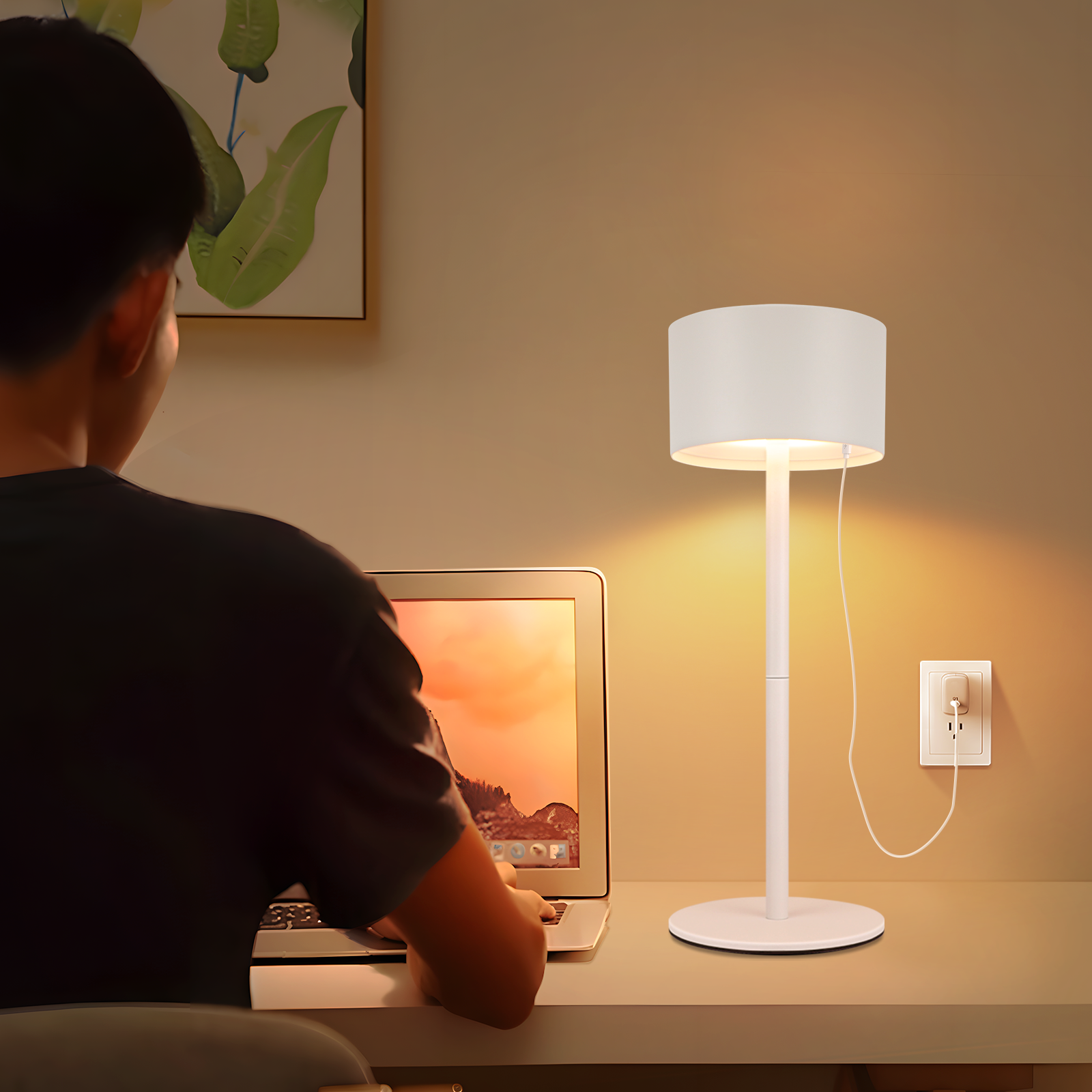 Osoba siedząca przy biurku korzystająca z laptopa z białą lampą w pobliżu.