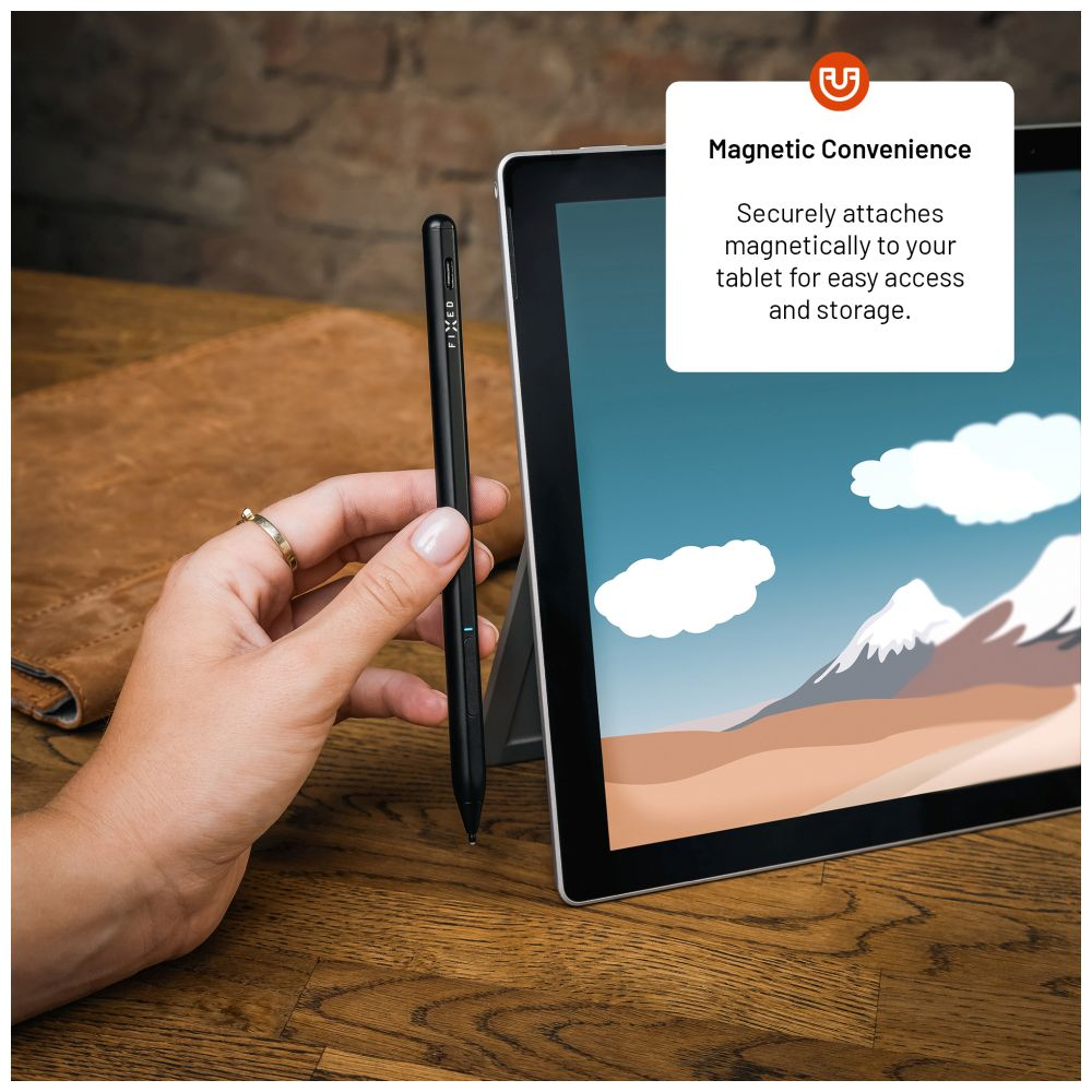 Hand hält schwarzen Stift neben Tablet, zeigt Landschaft, Holzoberfläche.