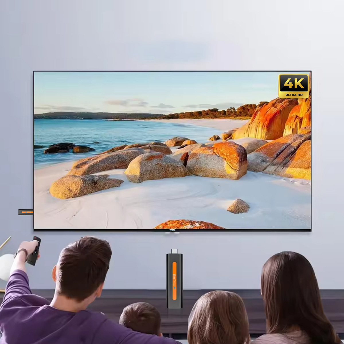 Rodzina ogląda telewizję. Ekran wyświetla scenę z plażą. Urządzenie do strumieniowania znajduje się przed ekranem.