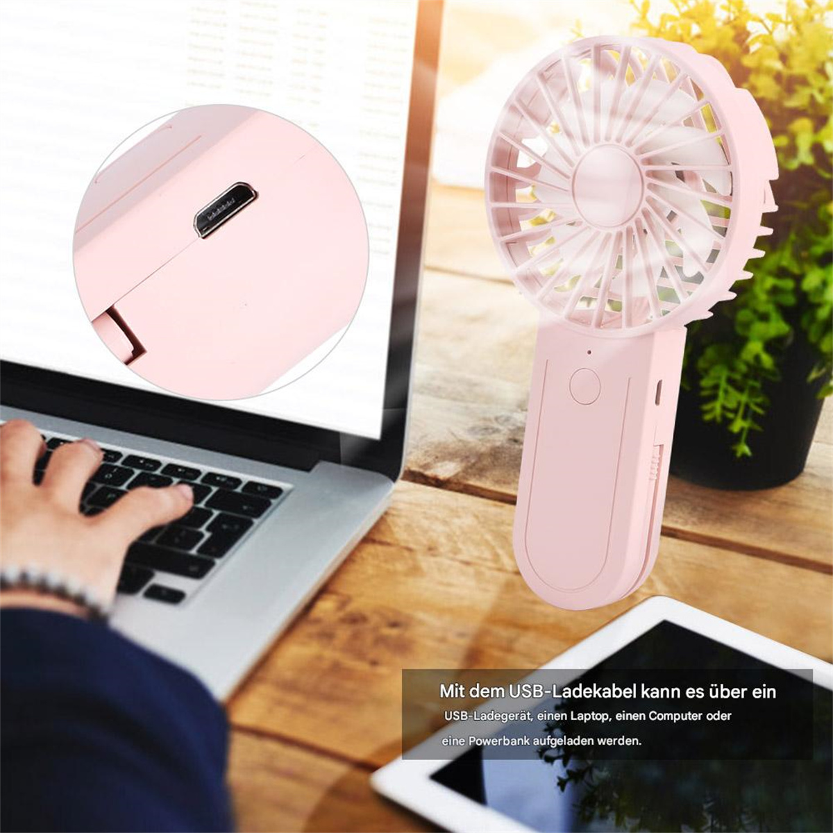 Ein pinkfarbener Handventilator mit USB-Anschluss, neben einem Laptop und einer Topfpflanze.