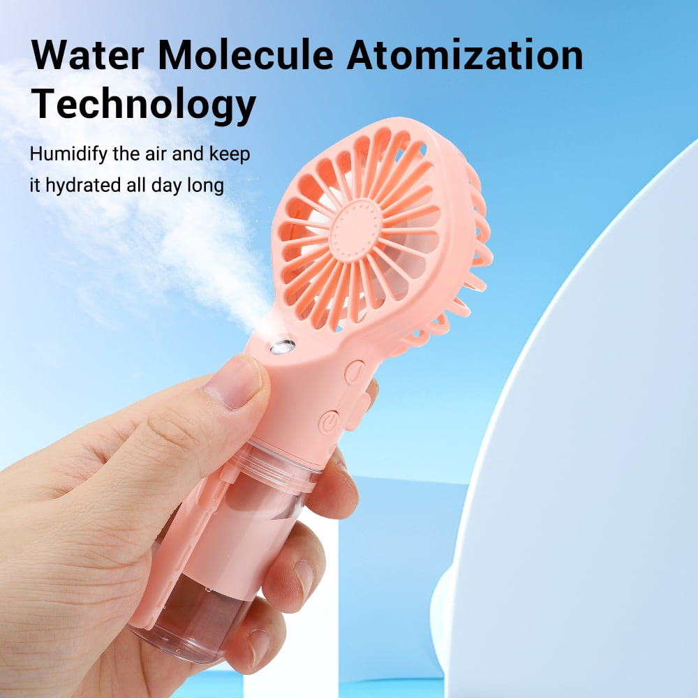 Eine Hand hält einen rosa-weißen tragbaren Ventilator, der Wassernebel gegen einen blauen Himmel sprüht.