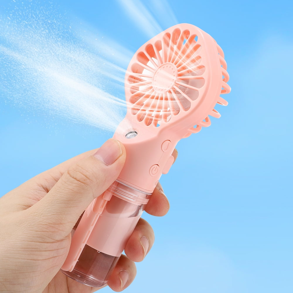 Eine Hand, die einen rosa Handventilator hält, der Nebel sprüht. Blauer Himmel im Hintergrund.