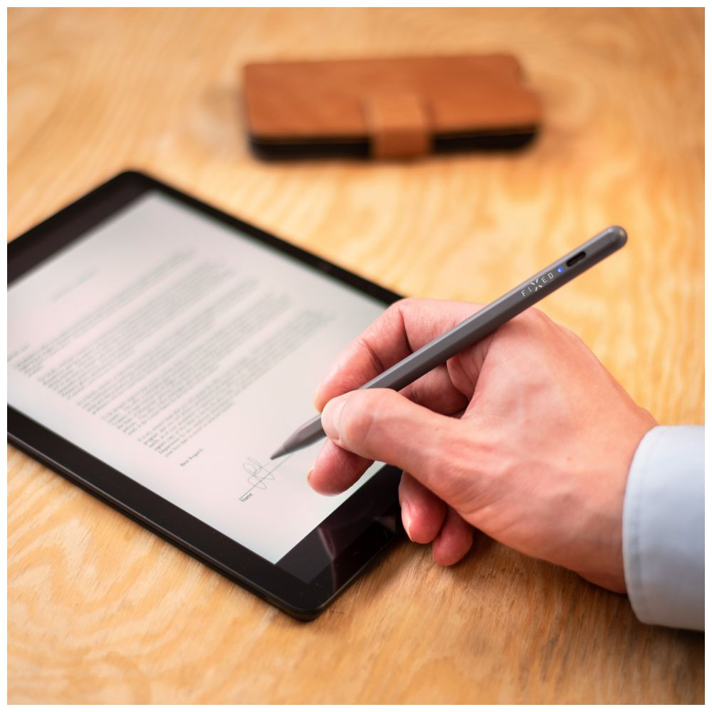 Eine Hand, die einen grauen Stylus hält und auf einem Tablet schreibt. Im Hintergrund ist ein braunes Etui.