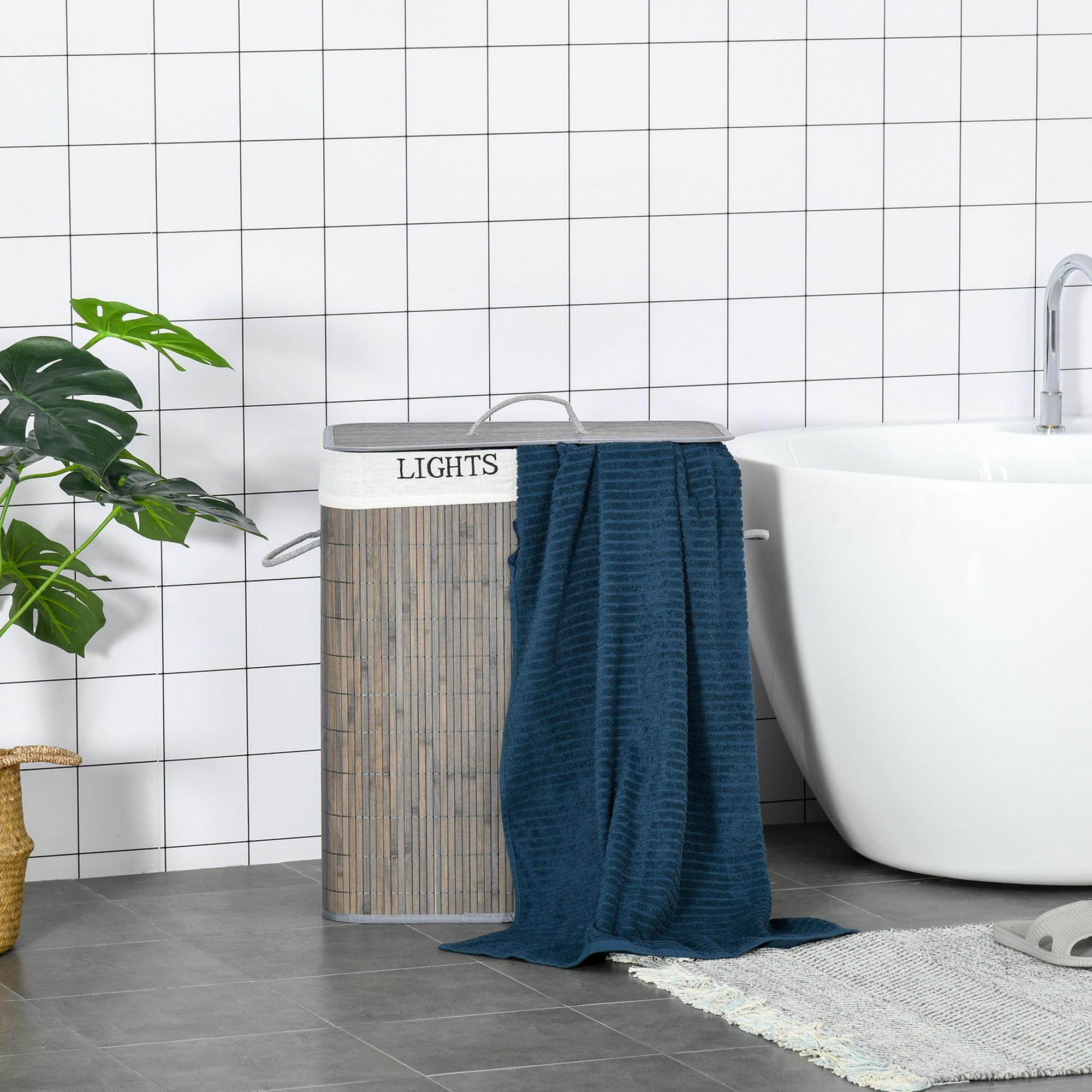 Wäschekorb mit einem blauen Handtuch, das darüber drapiert ist, in der Nähe einer weißen Badewanne. Pflanze und geflieste Wand.