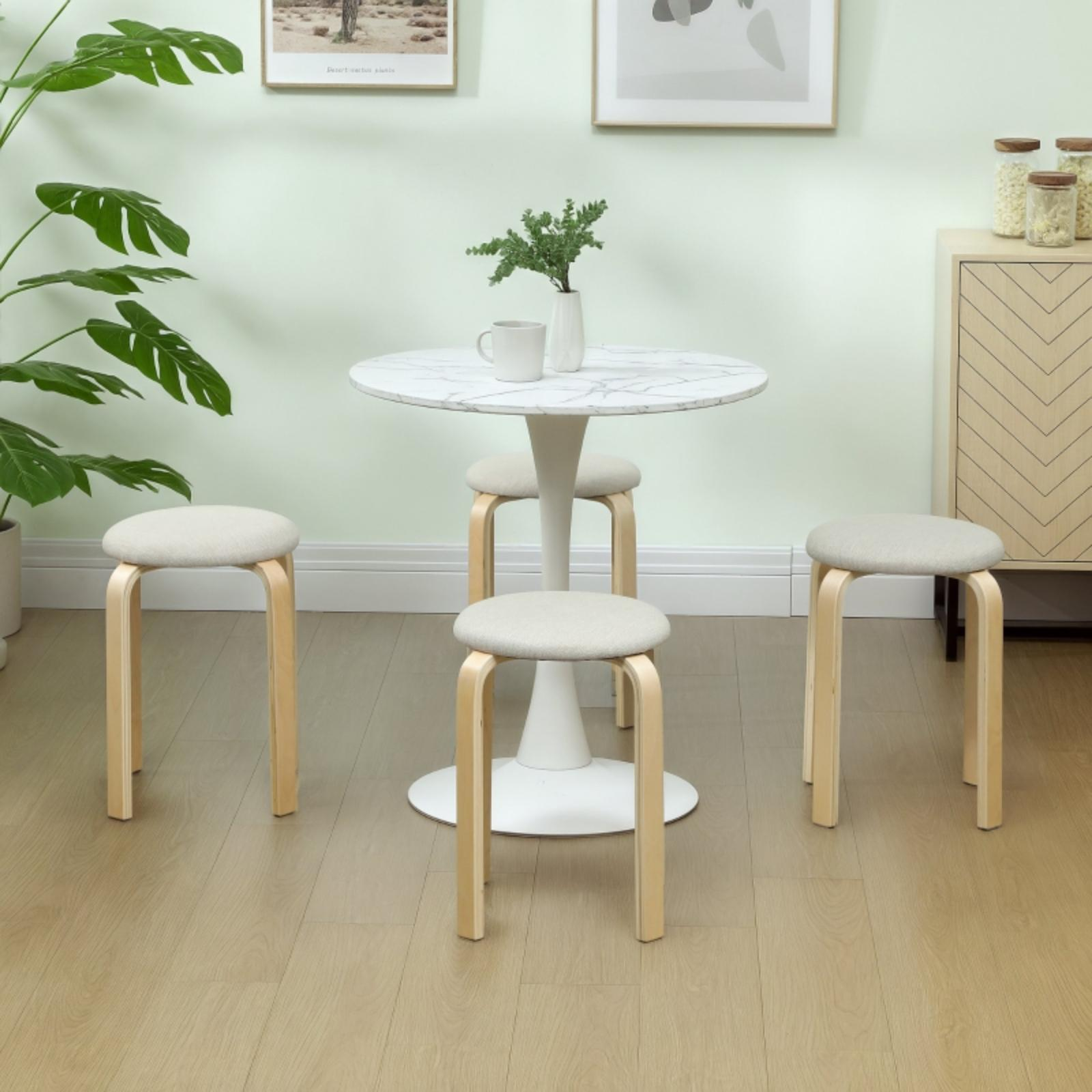 Vier helle Holzstühle um einen weißen runden Tisch. Eine Vase mit Grün steht in der Mitte des Tisches.