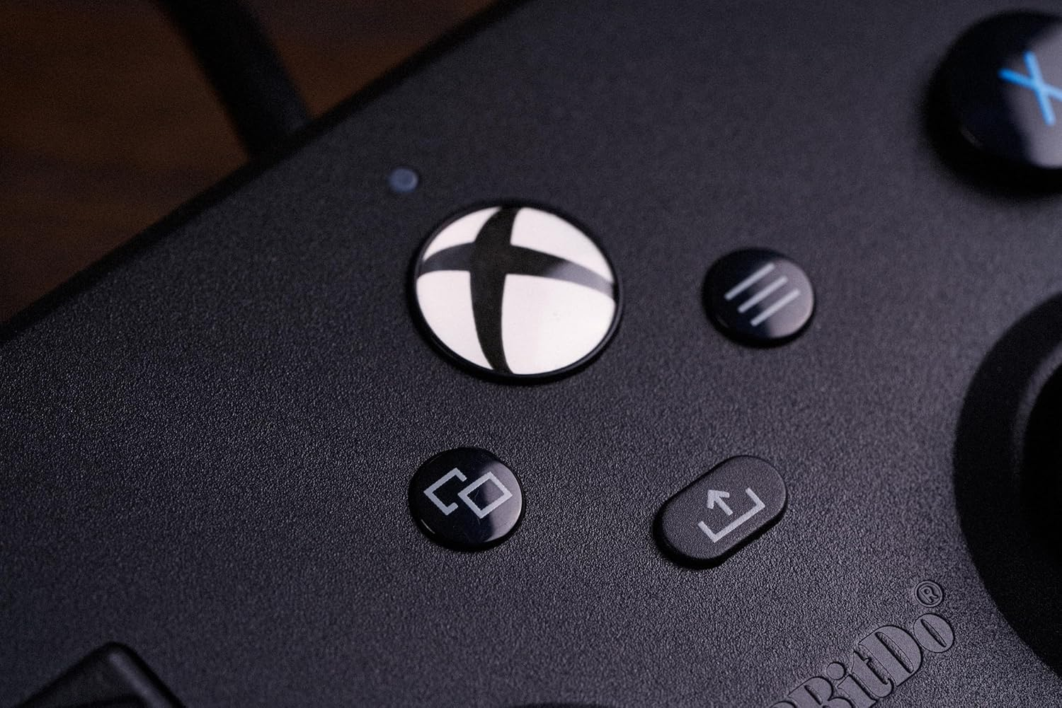 Zbliżenie czarnego gamepada. Pokazuje przyciski, w tym przycisk X i logo.