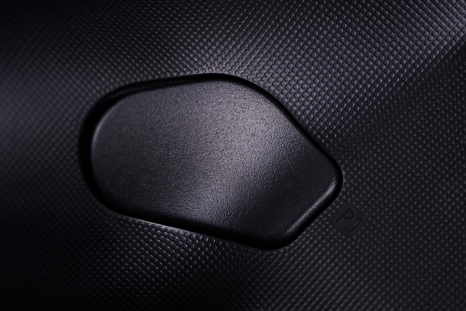 Zbliżenie czarnej, teksturowanej powierzchni z wypukłym owalem. Jest mały przycisk.