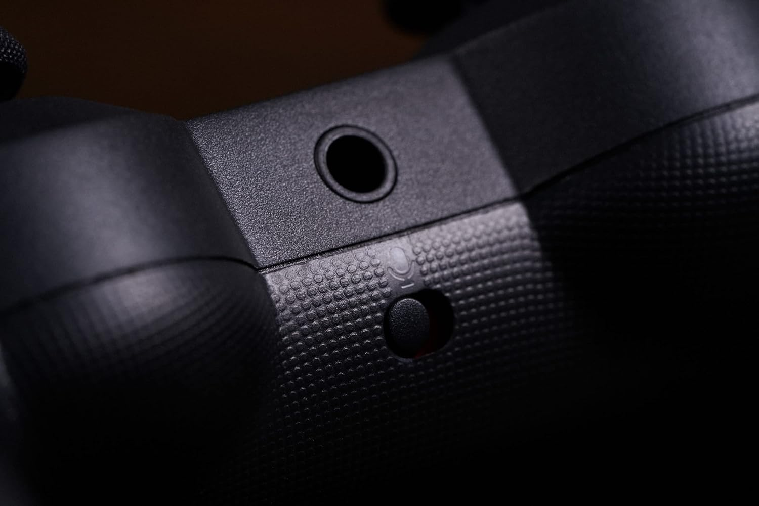 Zbliżenie czarnego gamepada. Zawiera gniazdo słuchawkowe i przycisk.