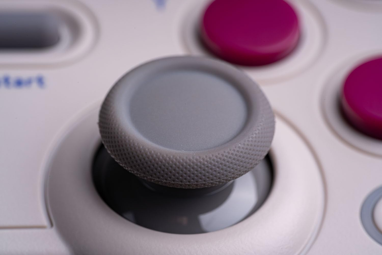 Zbliżenie szarego joysticka na kontrolerze do gier z białym korpusem i fioletowymi przyciskami.