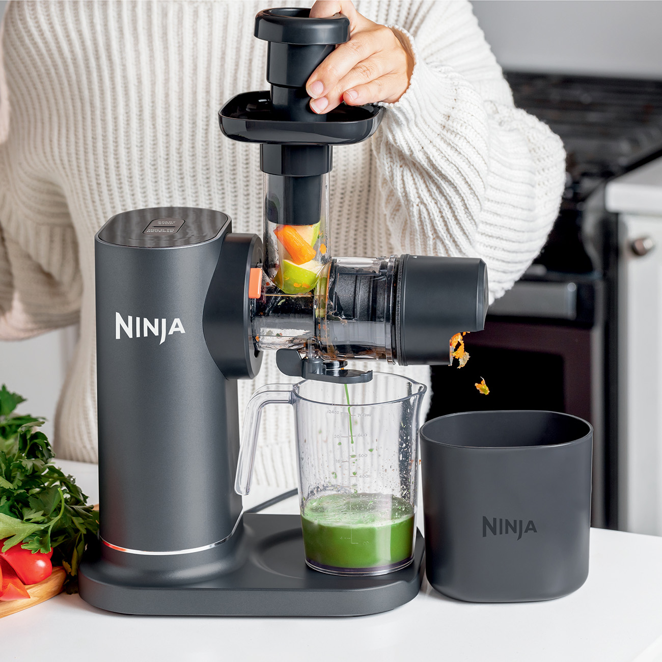 Person using a Ninja juicer. Green juice is being poured into a glass.