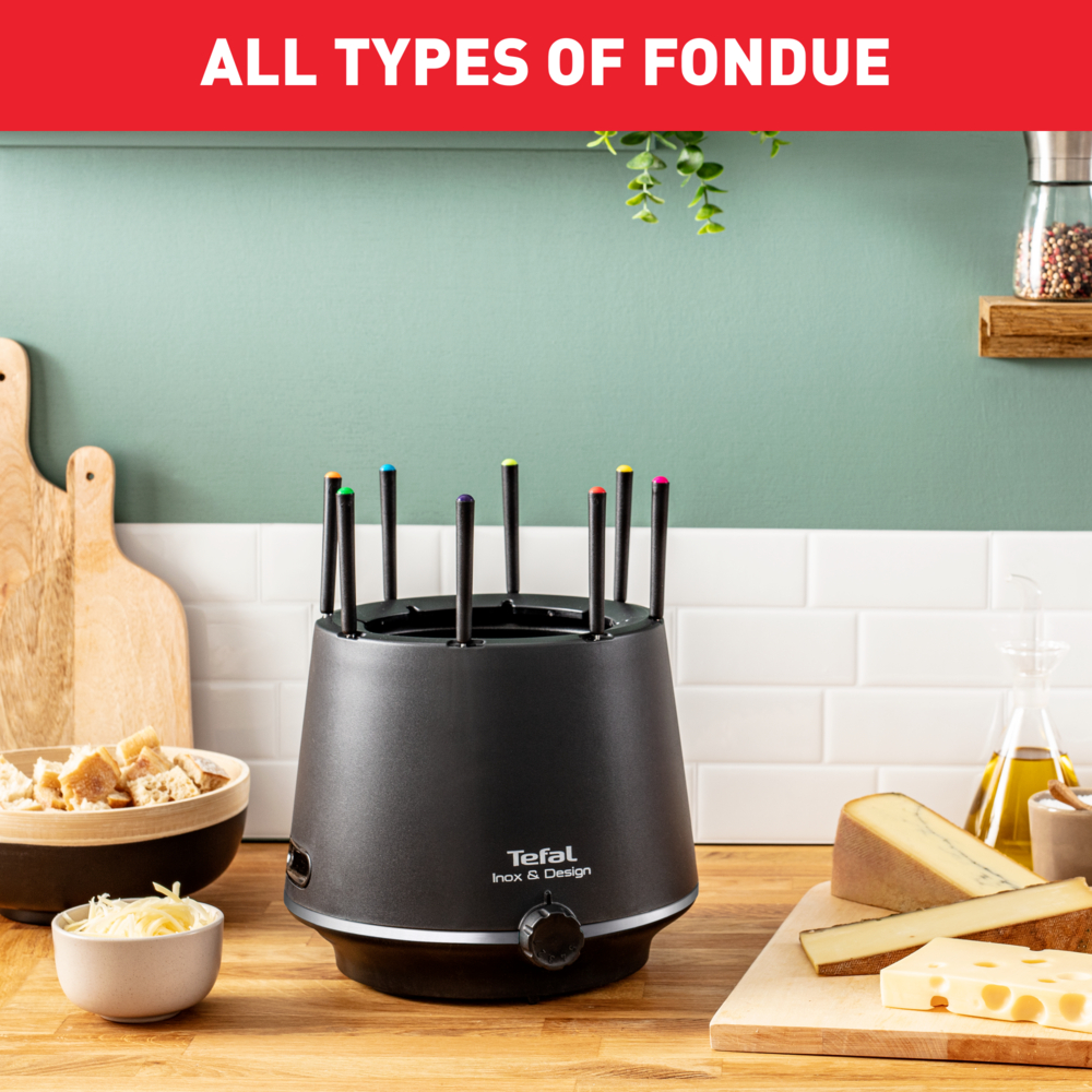 Czarny garnek do fondue z kolorowymi widelcami. Widoczna miska z serem, chlebem i butelką oleju.