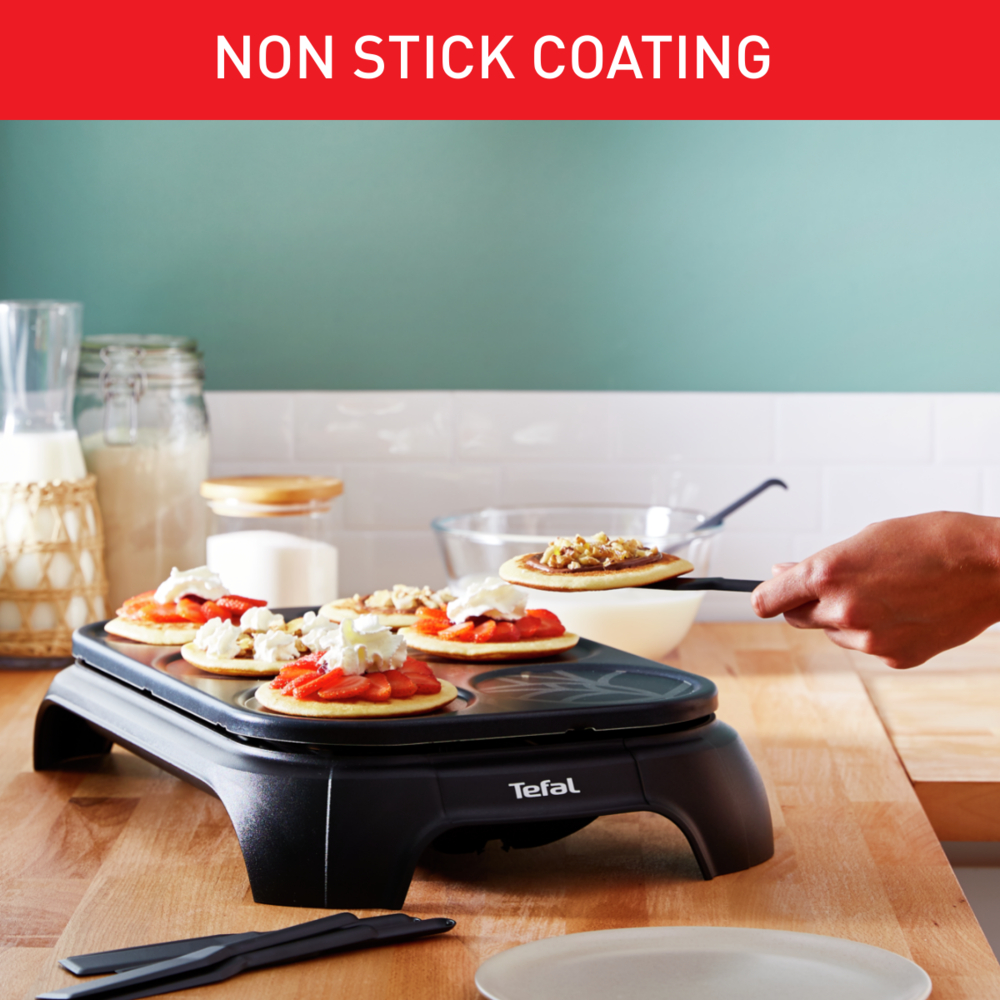 Maszyna do naleśników z naleśnikami posypanymi truskawkami i bitą śmietaną. Ręka trzymająca szpatułkę.