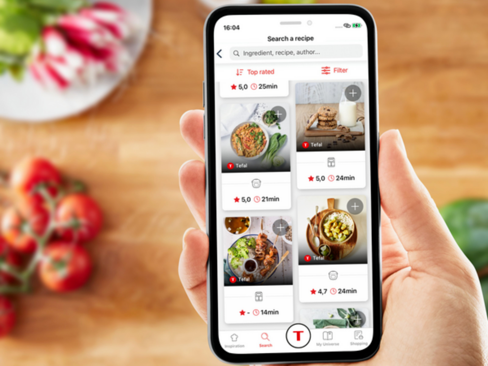 Ręka osoby trzymająca smartfon z opcjami przepisów na drewnianym stole.