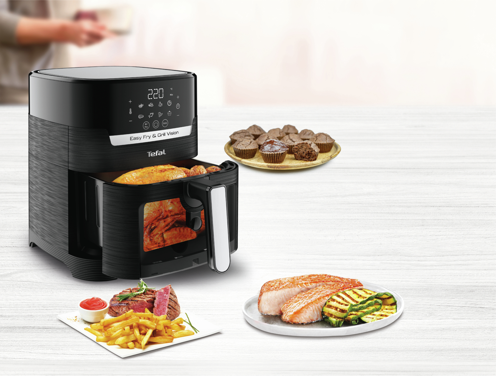 Eine schwarze Heißluftfritteuse mit verschiedenen Gerichten: Steak und Pommes, Muffins, gegrillter Lachs und Zucchini.