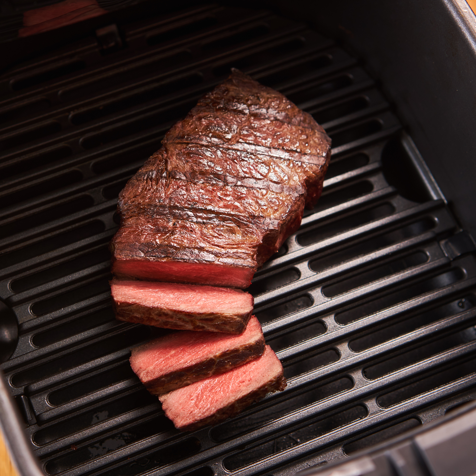 Geschnittenes, gekochtes Steak auf einem schwarzen Grill. Das Fleisch hat eine gebratene Außenseite und ist innen rosa.