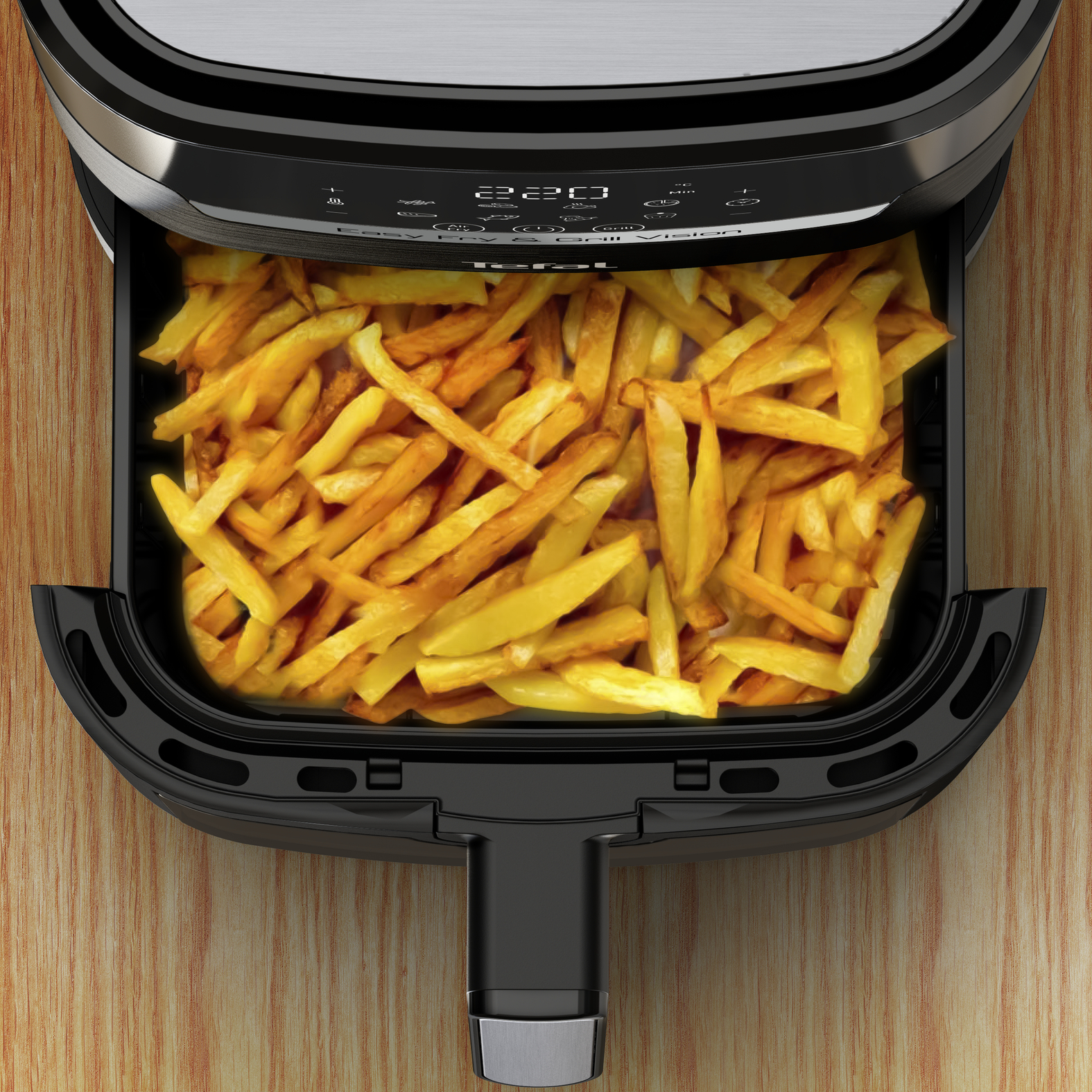 Draufsicht auf einen schwarzen Heißluftfritteusenkorb, gefüllt mit goldbraunen Pommes frites auf einer Holzoberfläche.
