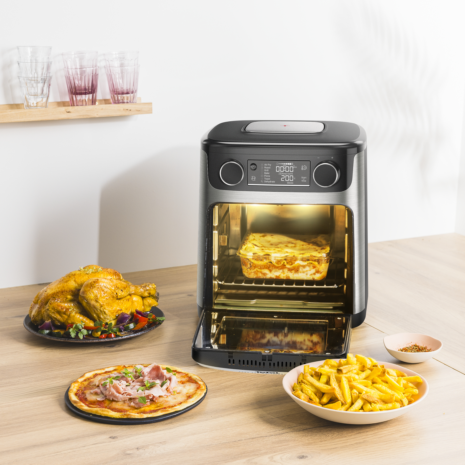 Czarna frytkownica powietrzna z przeszklonymi drzwiami oraz różnymi potrawami: lasagne, pizzą, kurczakiem i frytkami.