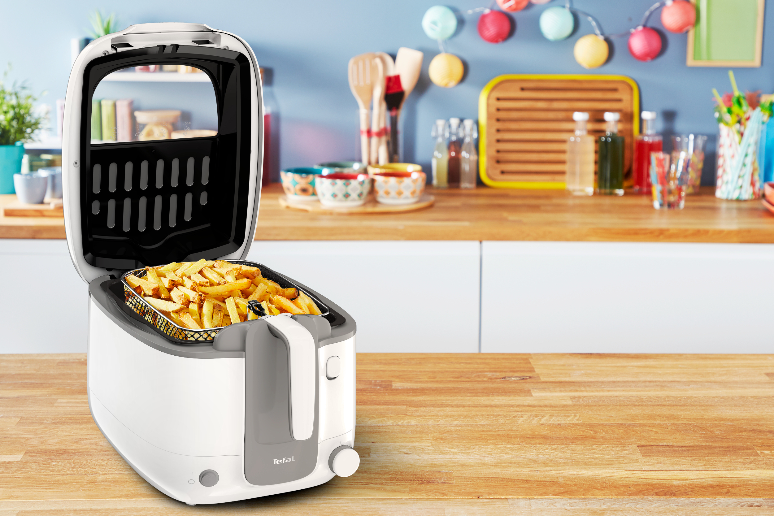 Freidora Tefal blanca con patatas fritas en la cesta, abierta. Fondo de cocina.