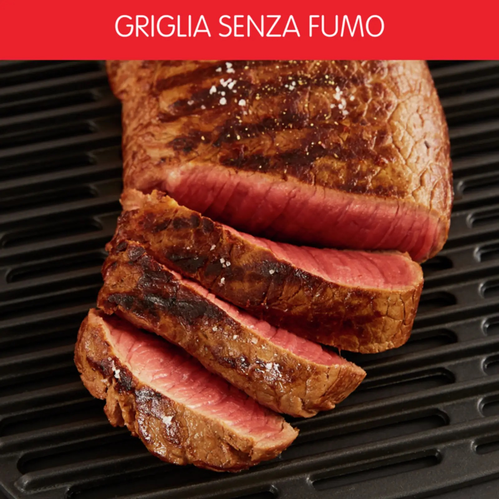 Pokrojony stek na czarnym grillu. Tekst 'GRIGLIA SENZA FUMO' jest nad stekiem na czerwono.