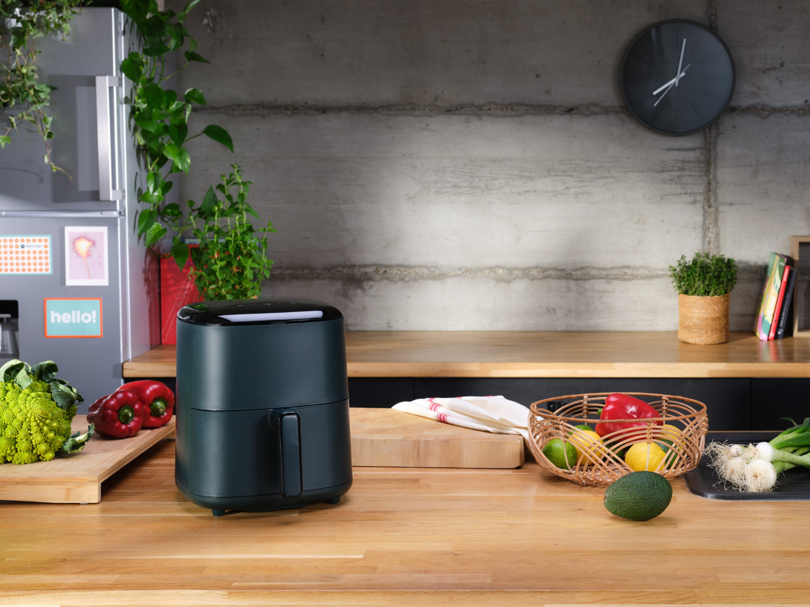 Ciemnozielona frytkownica na drewnianym stole. Warzywa i zegar w tle. Kuchnia.