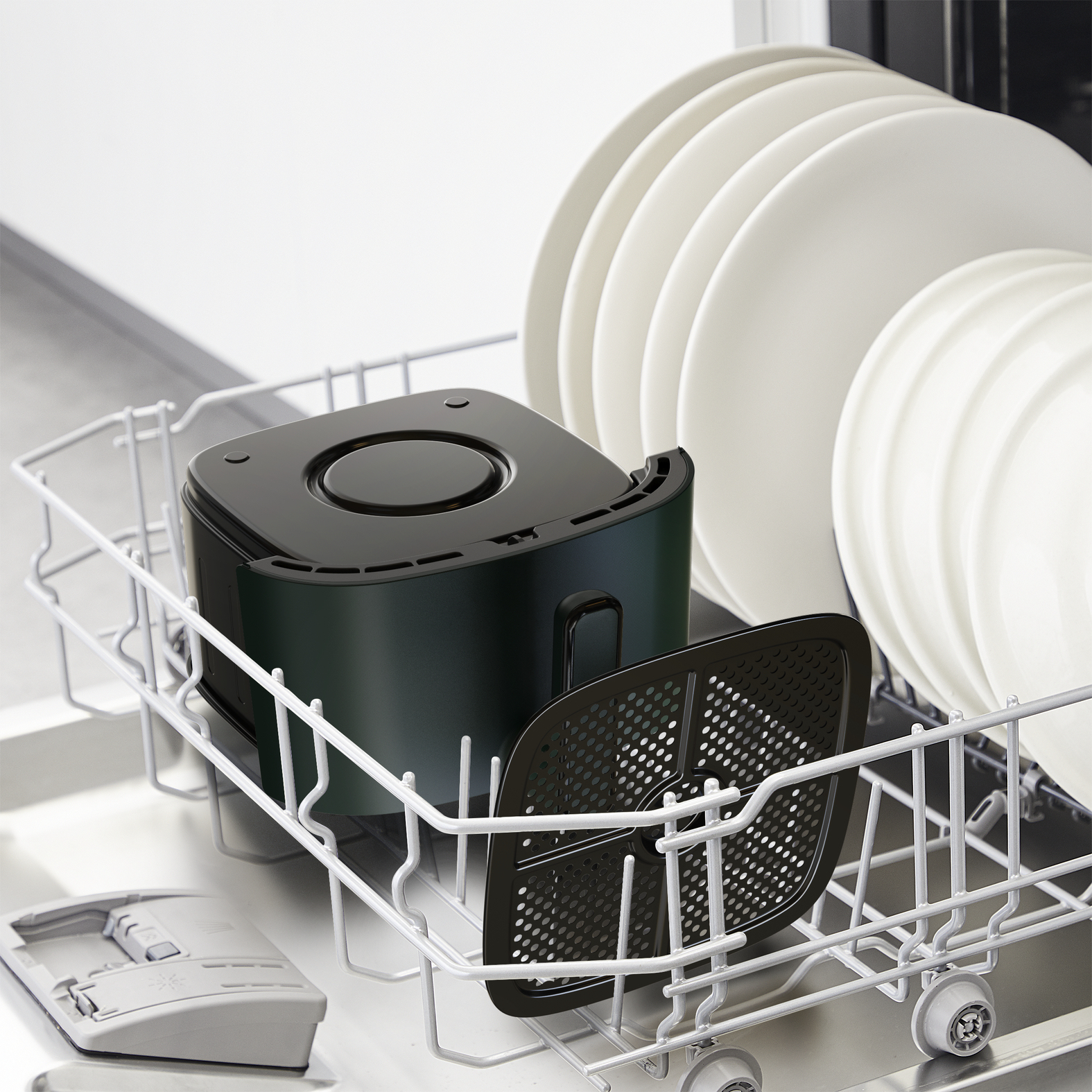 Czarne elementy frytkownicy w koszu zmywarki. Talerze w tle.