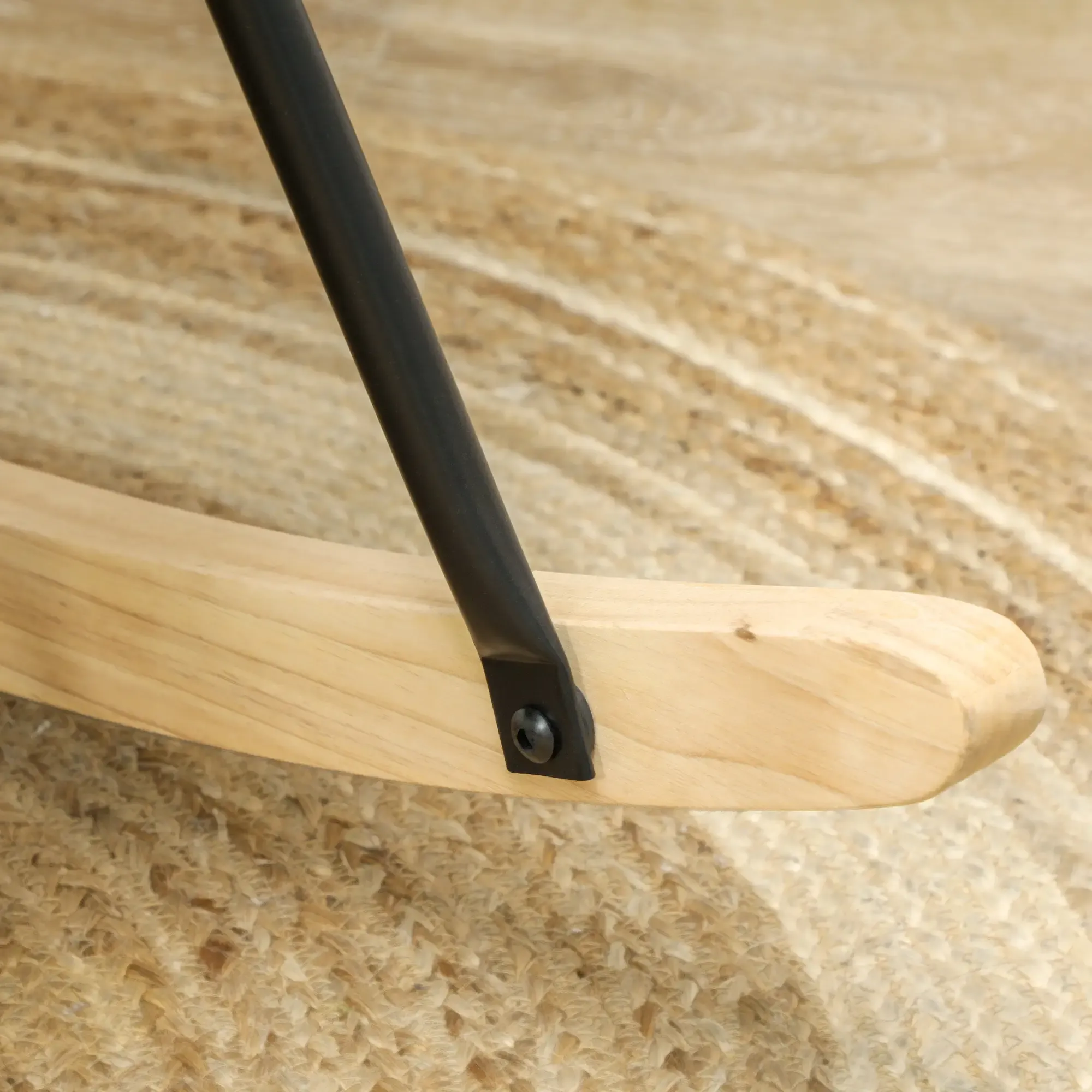 Nahaufnahme einer Holzwippbasis, schwarzer Metallstütze und einem strukturierten beigefarbenen Teppich.