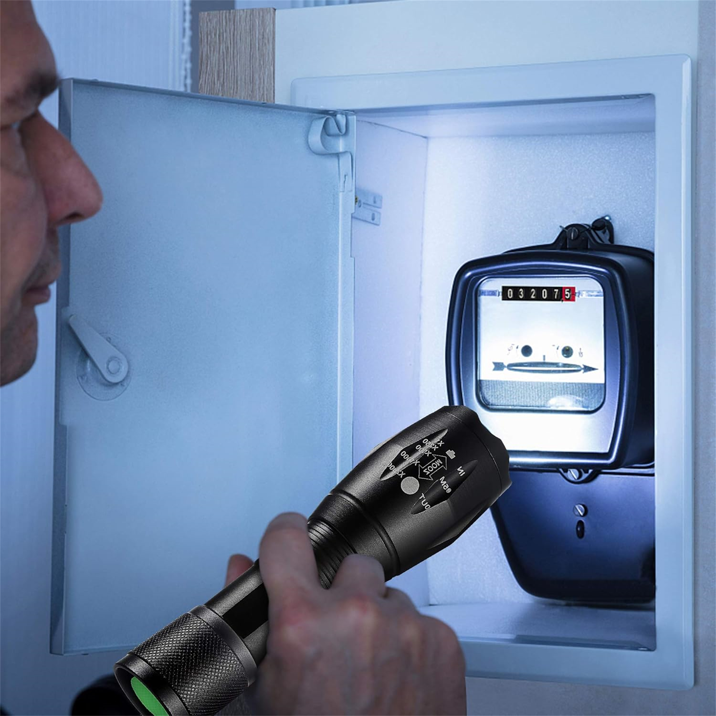 Eine Person leuchtet mit einer Taschenlampe auf einen Stromzähler in einem weißen Schrank. Der Zähler zeigt Zahlen.