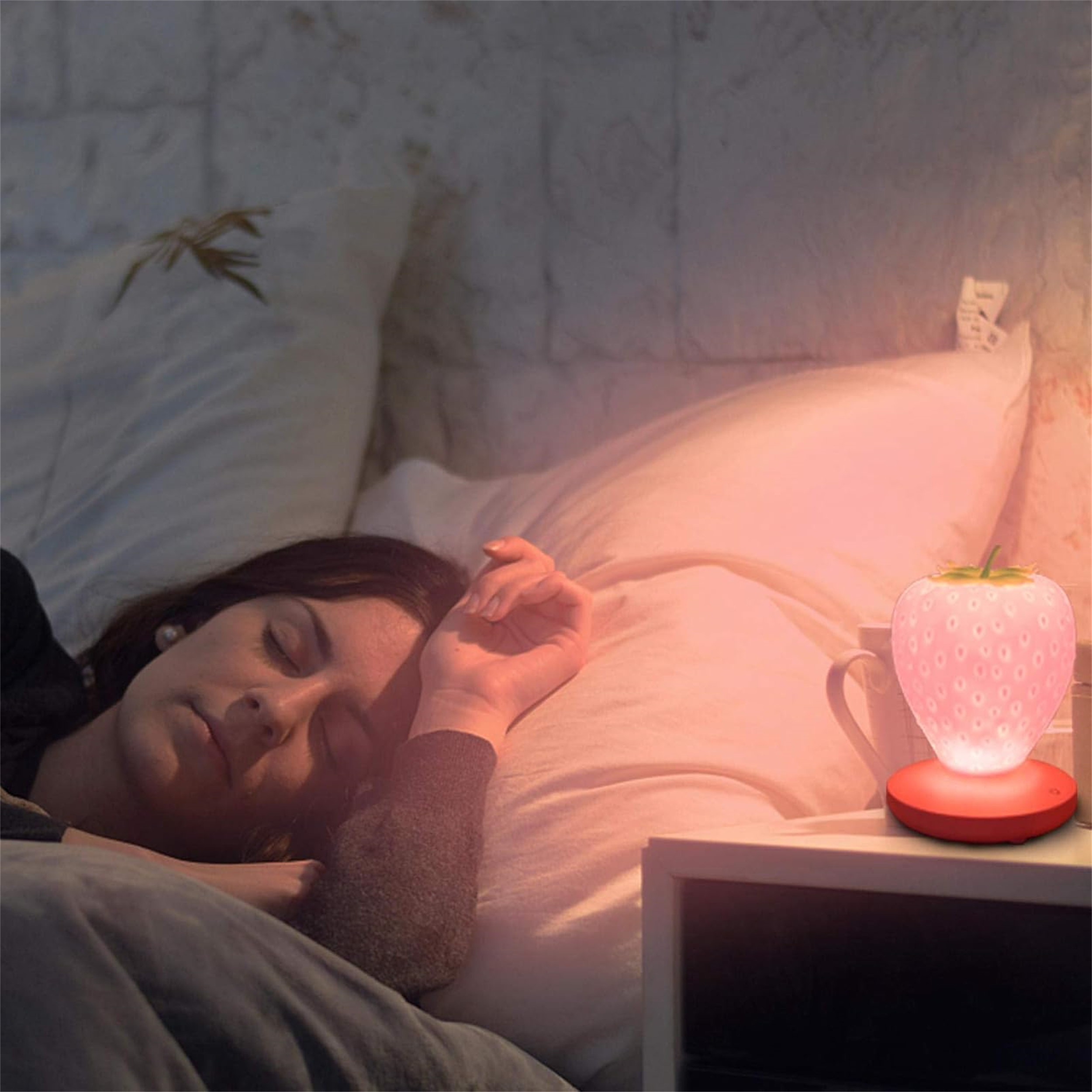 Eine Frau schläft im Bett. Eine erdbeerförmige Lampe leuchtet auf dem Nachttisch. Sanftes Licht erhellt den Raum.