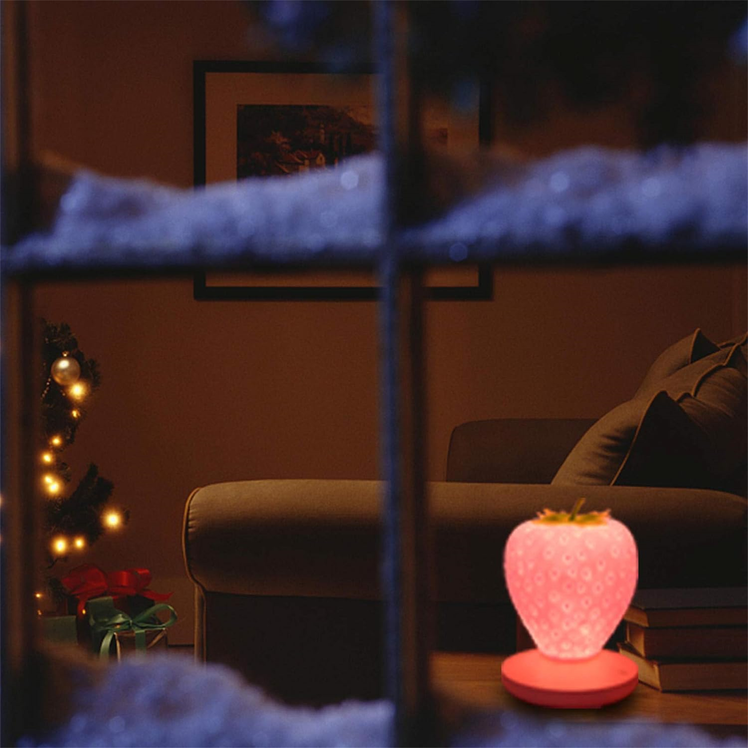 Eine erdbeerförmige Lampe leuchtet rosa in einem Raum. Ein Weihnachtsbaum und Geschenke sind sichtbar, im Hintergrund ein Sofa.