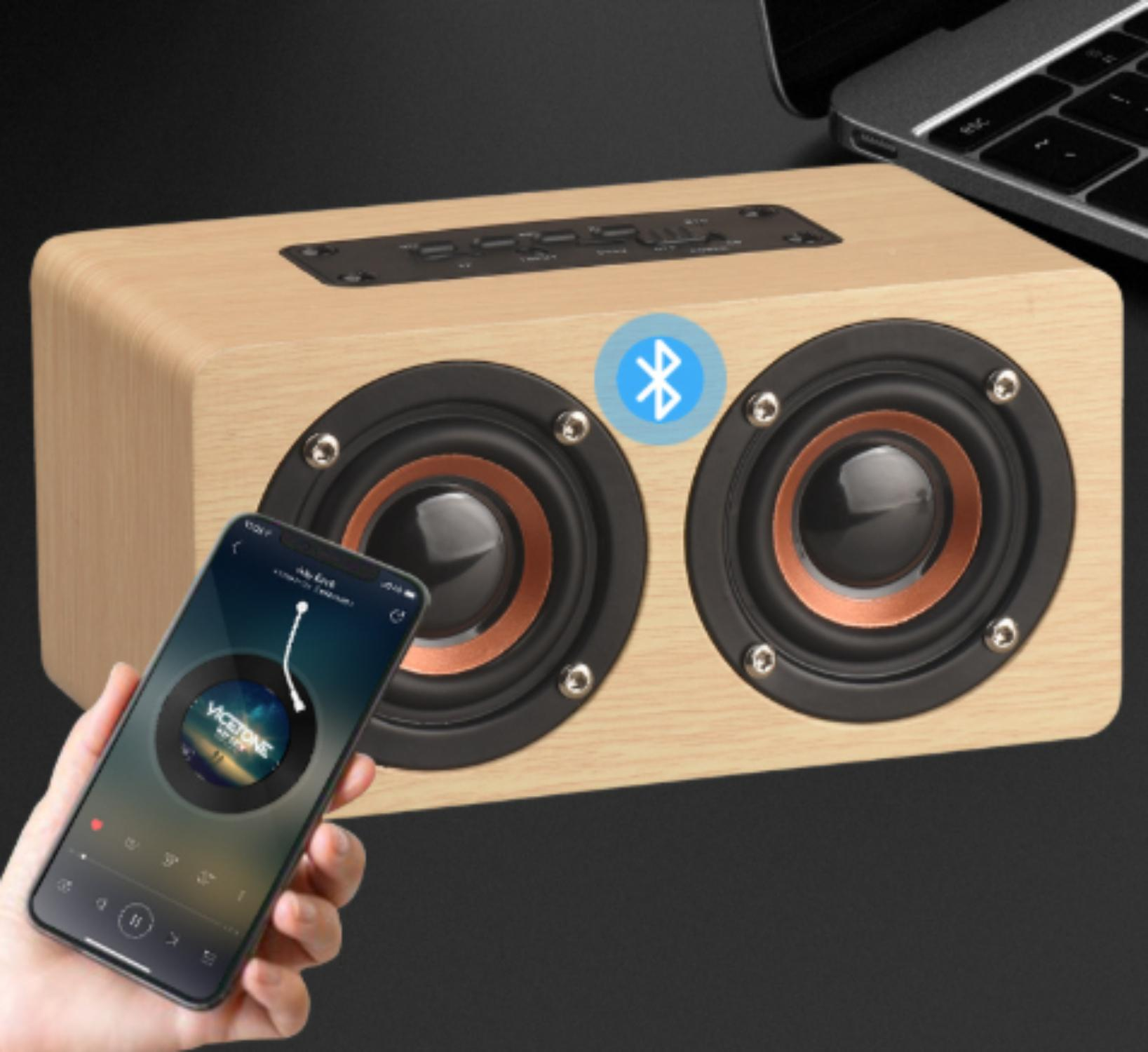 Holzlautsprecher mit zwei Lautsprechern, einem Musik abspielenden Telefon und einem Laptop im Hintergrund. Bluetooth-Symbol sichtbar.