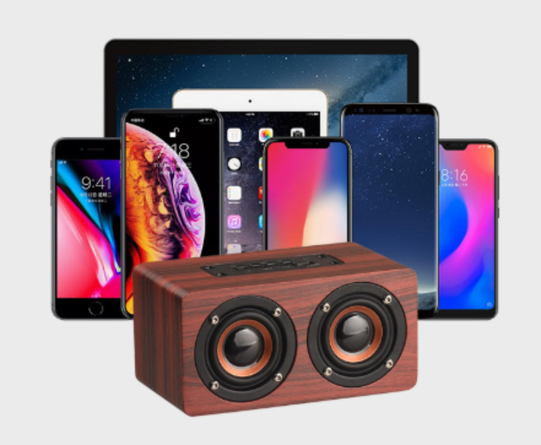 Ein hölzerner Lautsprecher mit zwei runden Lautsprechern befindet sich vor mehreren Smartphones und einem Tablet. Der Hintergrund ist weiß.