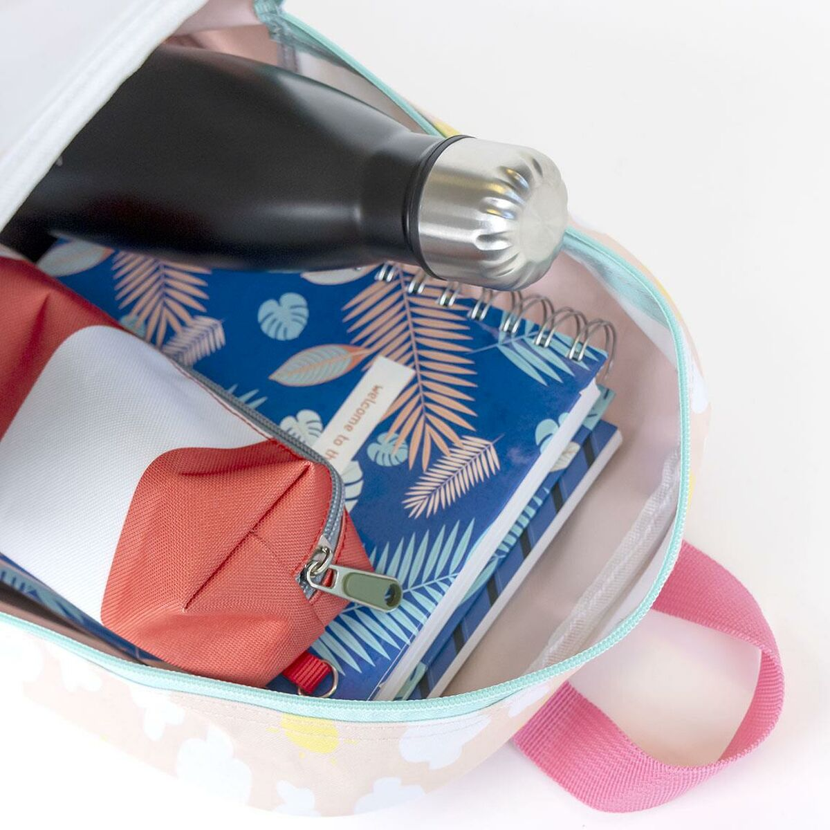 Rucksack gefüllt mit einer schwarzen Wasserflasche, einem roten Federmäppchen und blauen Notizbüchern. Rosa Griff. Die Tasche ist beige mit Wolken.