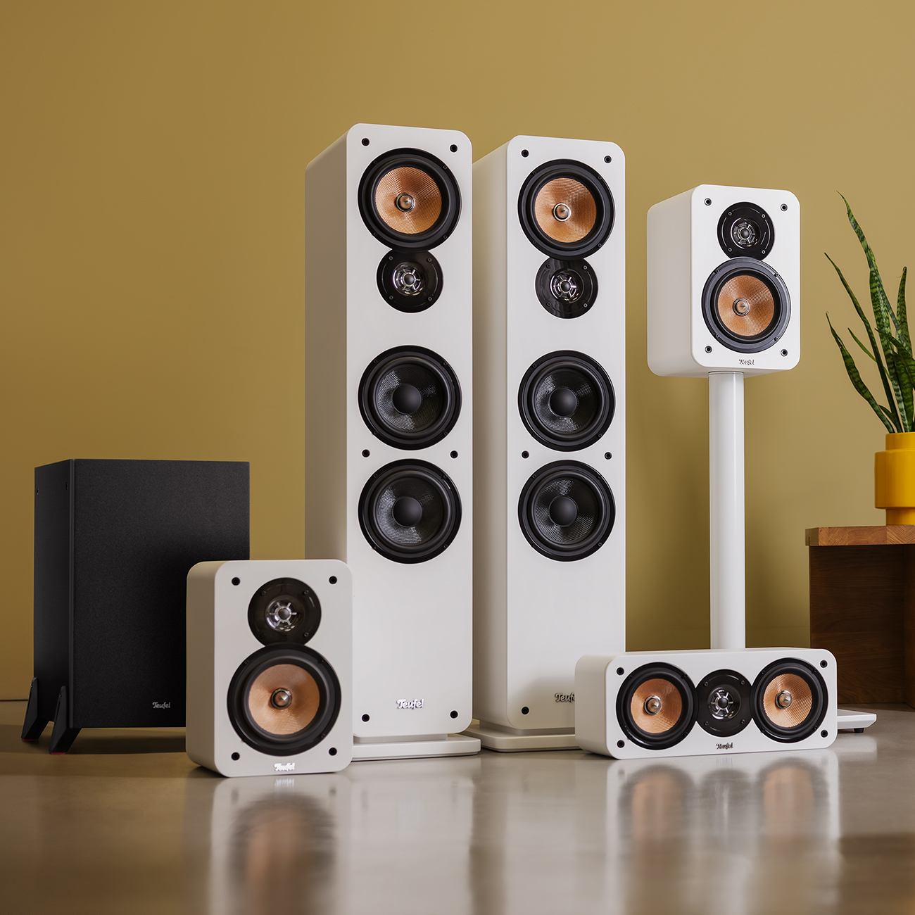 A set of white speakers with brown speakers, including a subwoofer. They are placed on a shiny floor, with a yellow wall behind them.