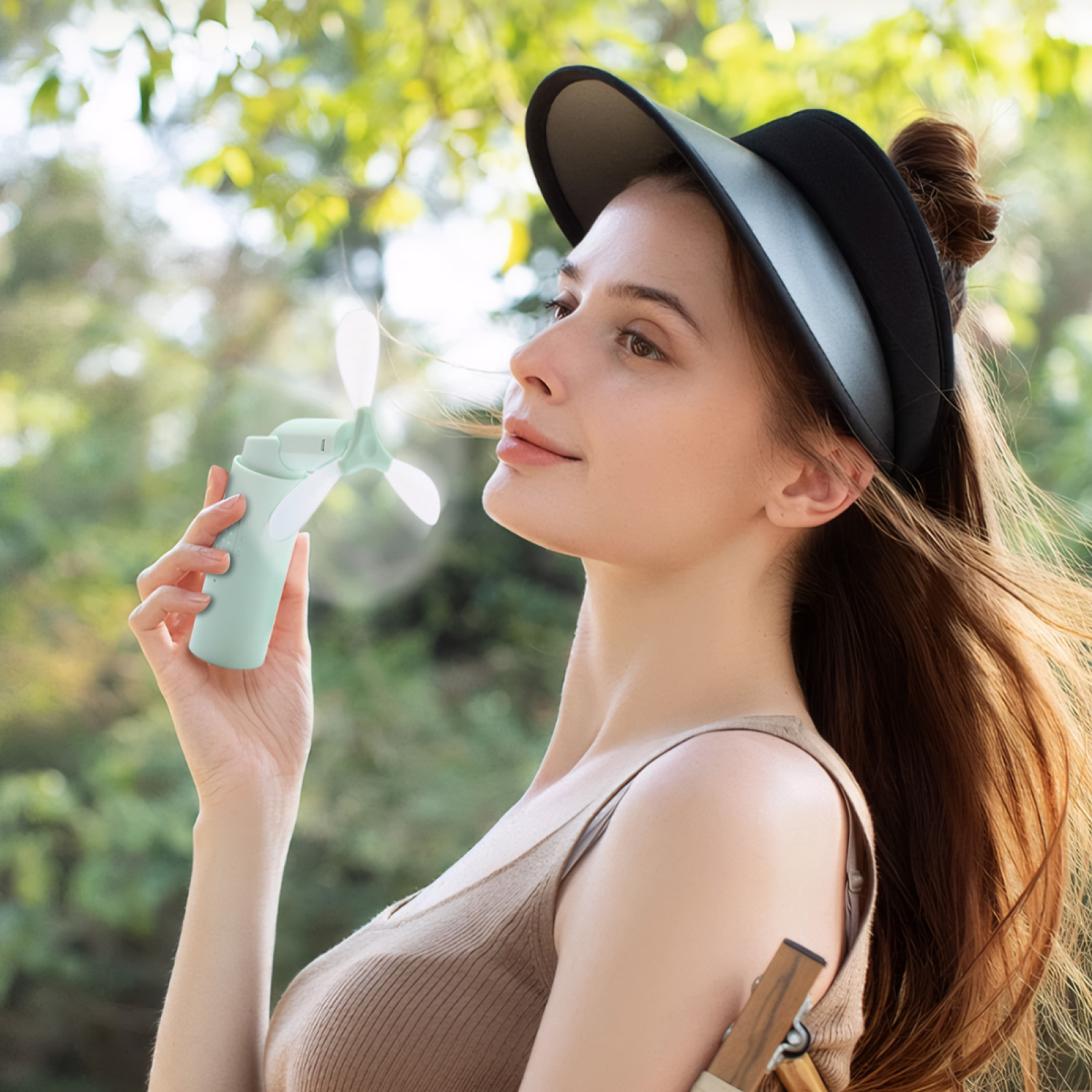 Eine Frau hält einen Minzlüfter und trägt einen Visor. Sie ist draußen mit grünem Laub im Hintergrund.