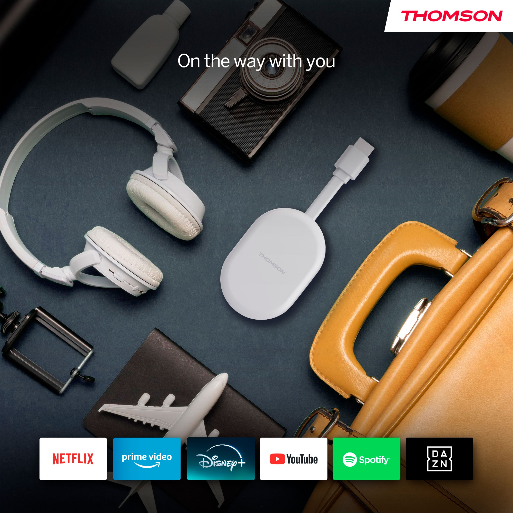 Auriculares blancos, un dispositivo blanco, una maleta y logotipos de aplicaciones de transmisión en una superficie azul. Logotipo Thomson visible.