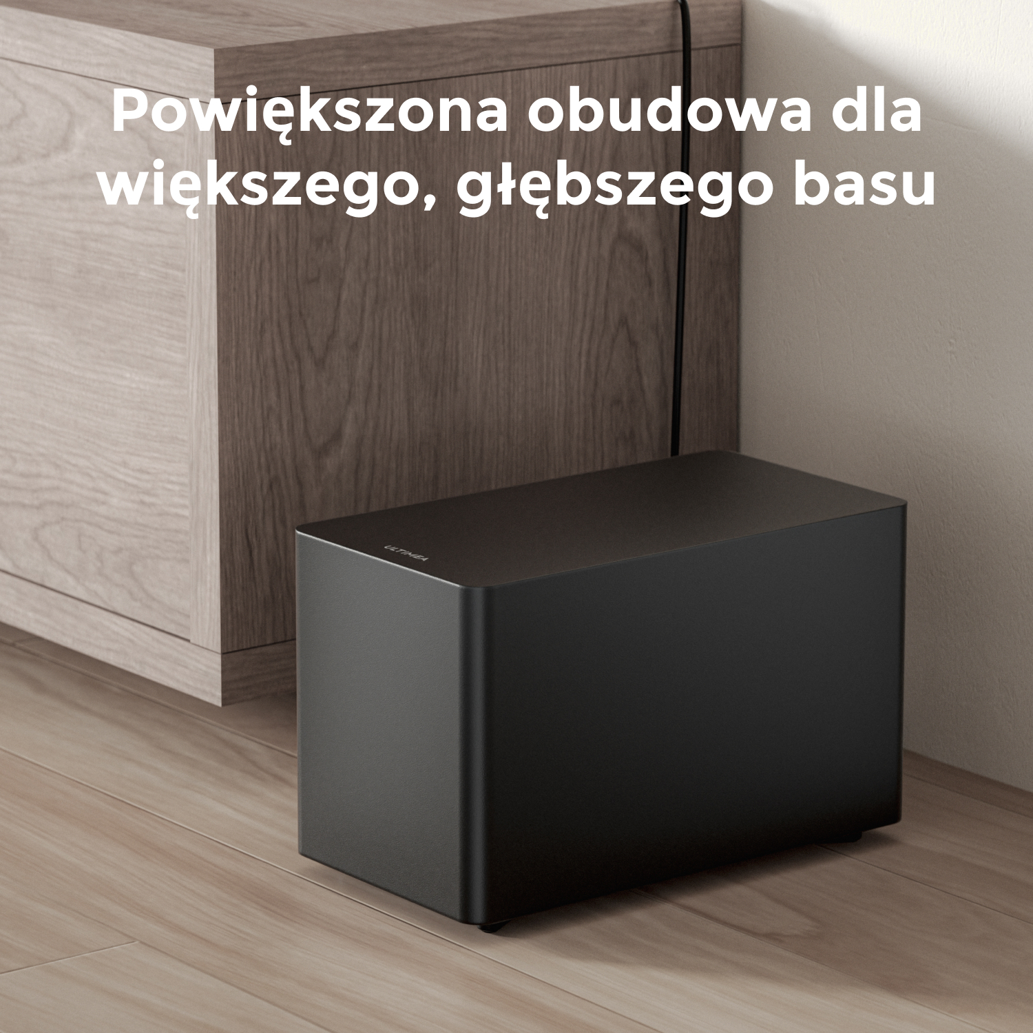 Czarny subwoofer na drewnianej podłodze obok drewnianej szafki. Tekst: Powiększona obudowa dla głębszego basu.