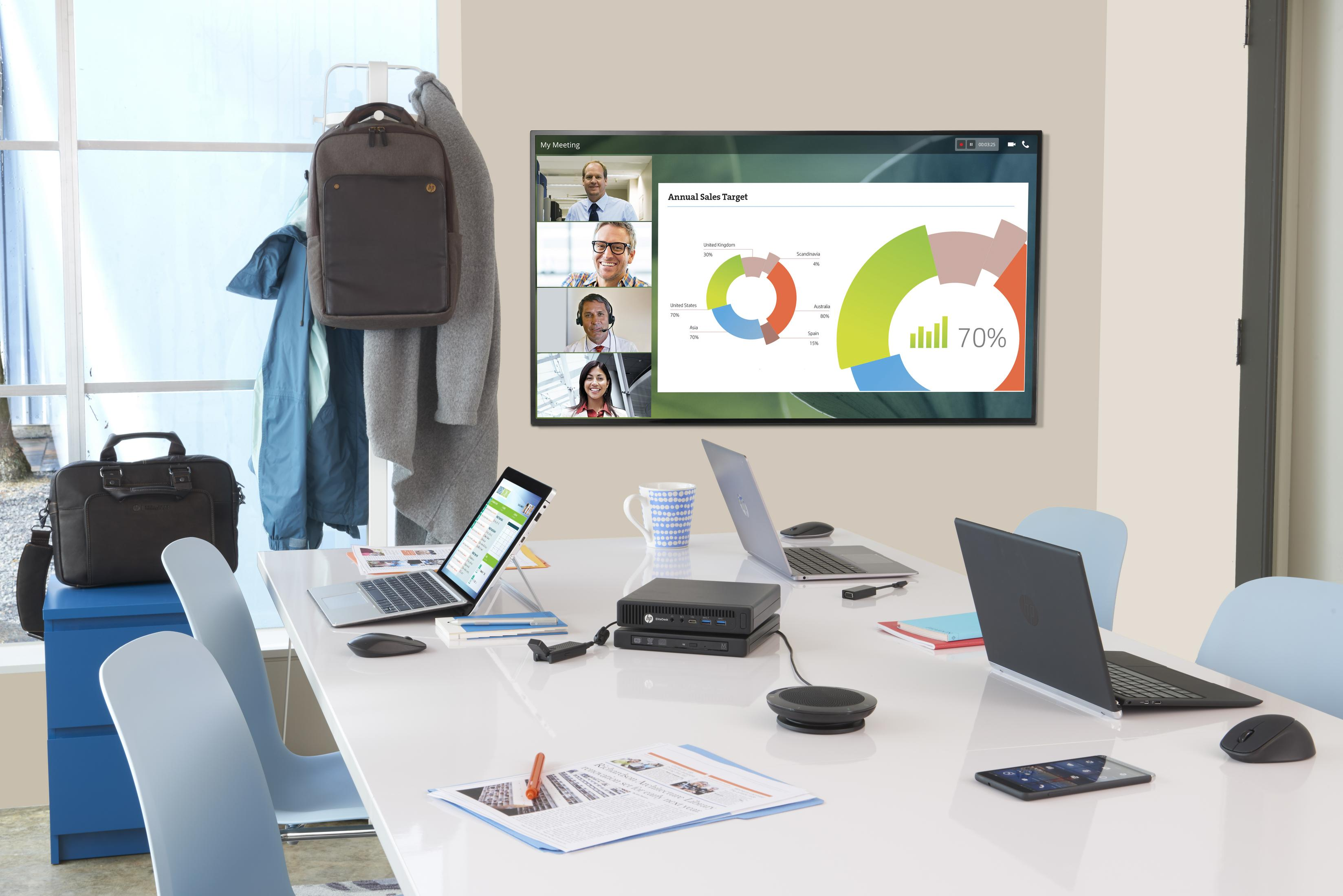 Ein Konferenzraum zeigt ein Meeting auf dem Bildschirm. Laptops, eine Tasche und Mäntel sind ebenfalls sichtbar.