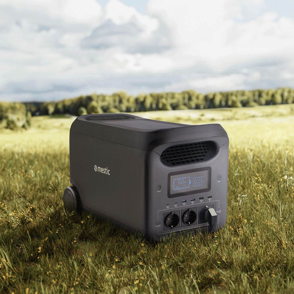 A black Mestic power station sits on grassy field. Display shows 60% charge. Forest in the background. Overcast sky.
