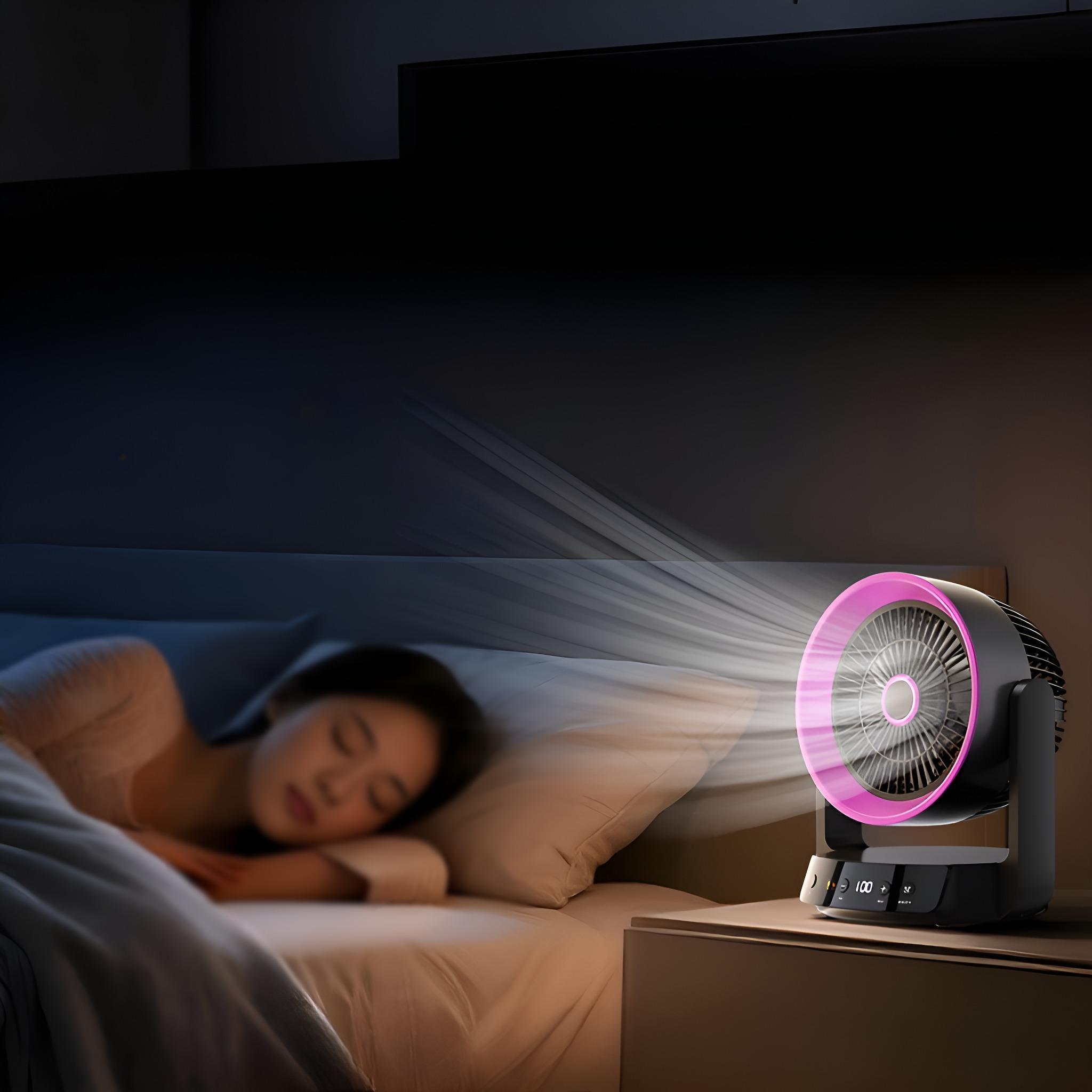 Eine Frau schläft im Bett. Ein Ventilator mit pinkfarbenem Ring auf einem Nachttisch bläst Luft. Dunkler Raum.