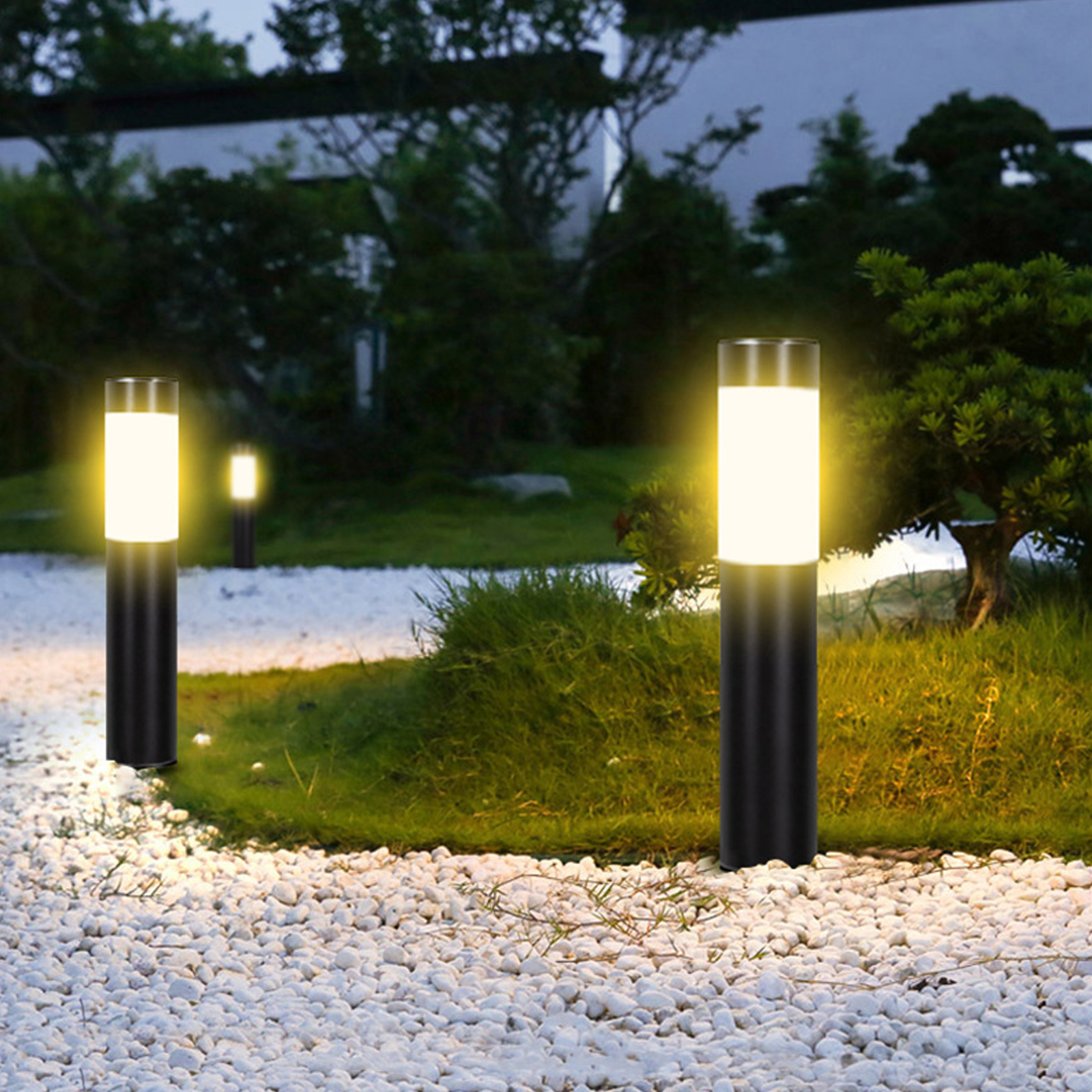 Nachtszenen im Freien mit leuchtenden, zylindrischen schwarzen Lampen. Weiße Steine im Vordergrund und grünes Gras im Hintergrund.