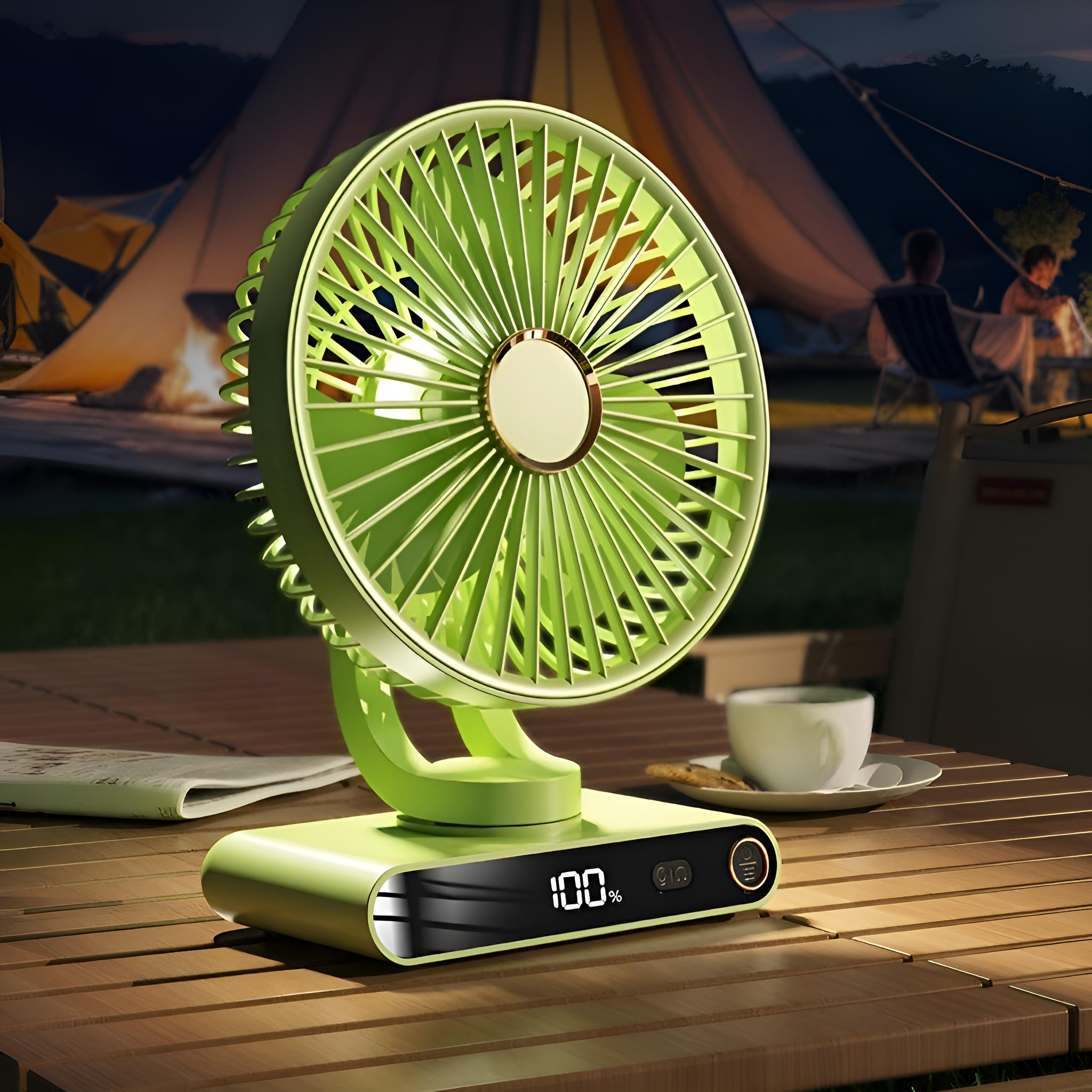 Ein grüner tragbarer Ventilator auf einem Holztisch, Anzeige zeigt 100%. Im Hintergrund ein Campingplatz bei Nacht.