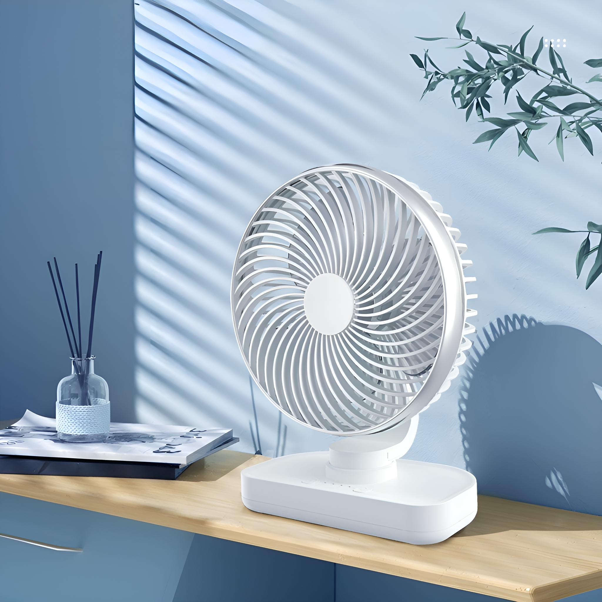 Weißer Ventilator auf Holzoberfläche, blauer Wandhintergrund. Schilfdiffusor und Buch sind ebenfalls vorhanden. Natürliches Licht.
