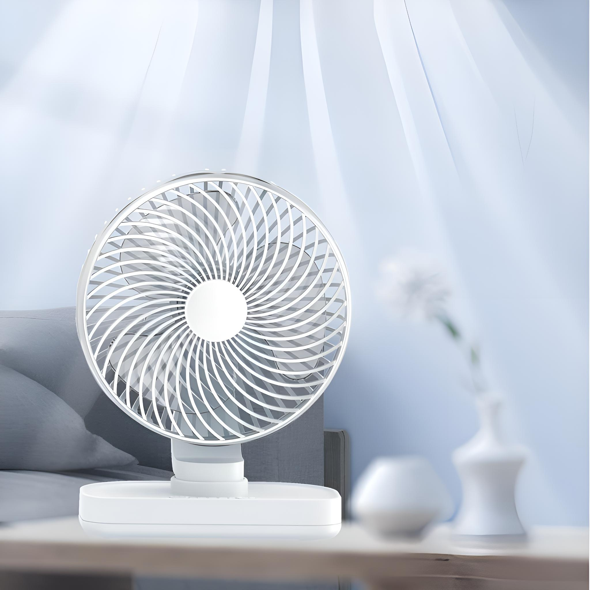 Ein weißer Tischventilator auf einem Tisch. Eine weiße Vase mit einer Blume und ein kleines weißes Objekt sind verschwommen im Hintergrund.