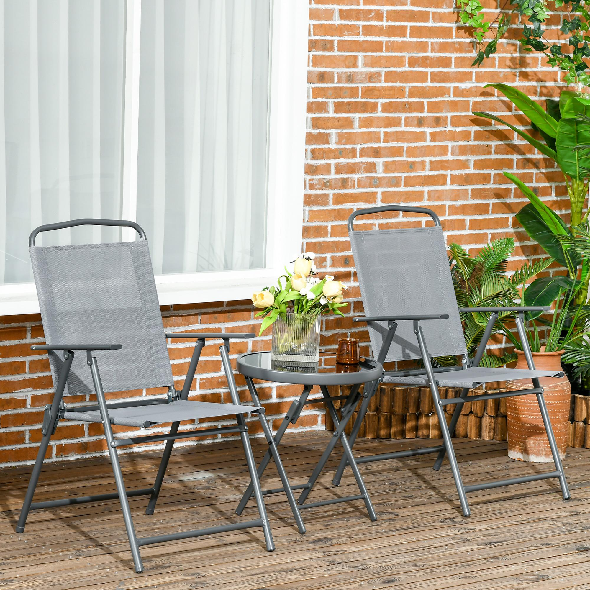 Zwei graue Klappstühle und ein kleiner Tisch auf einer Holzterrasse, vor einer Backsteinmauer und einem Fenster.