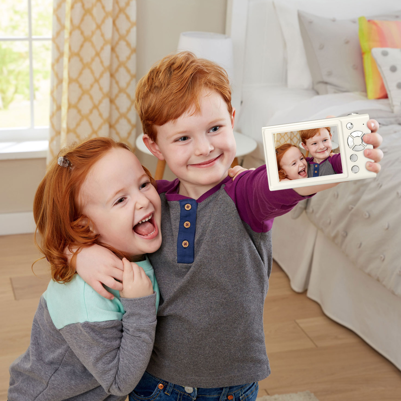 Zwei rothaarige Kinder machen ein Selfie mit einer Kamera. Eines lacht. Schlafzimmerhintergrund.