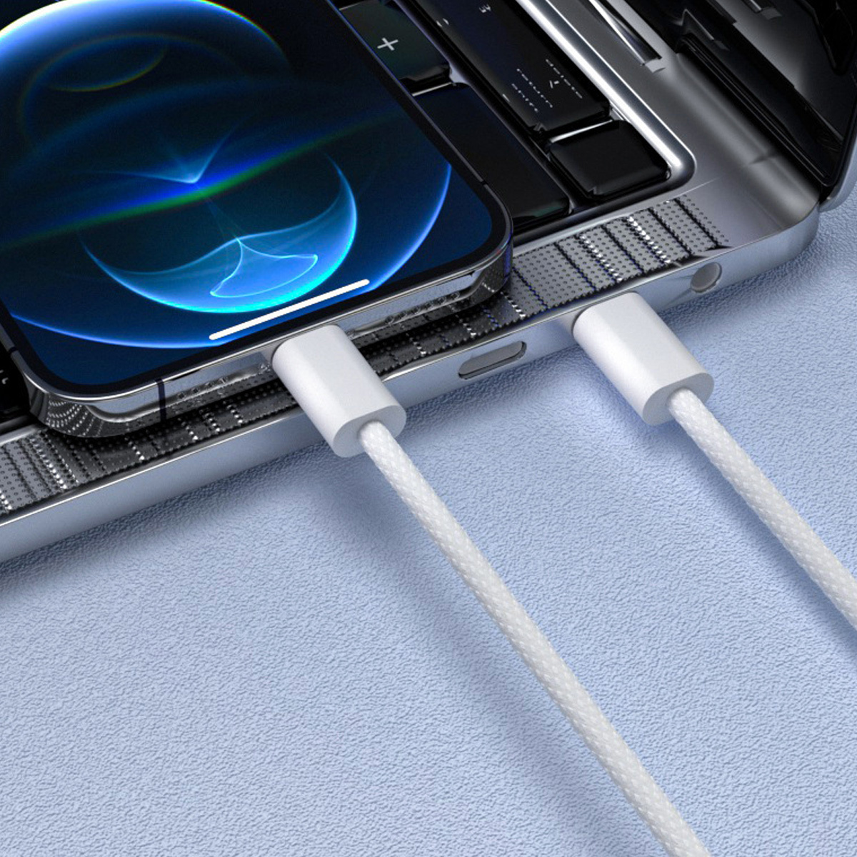 Ein Smartphone wird über ein weißes Kabel von einem Laptop aufgeladen. Der Telefonbildschirm zeigt ein blaues abstraktes Bild.