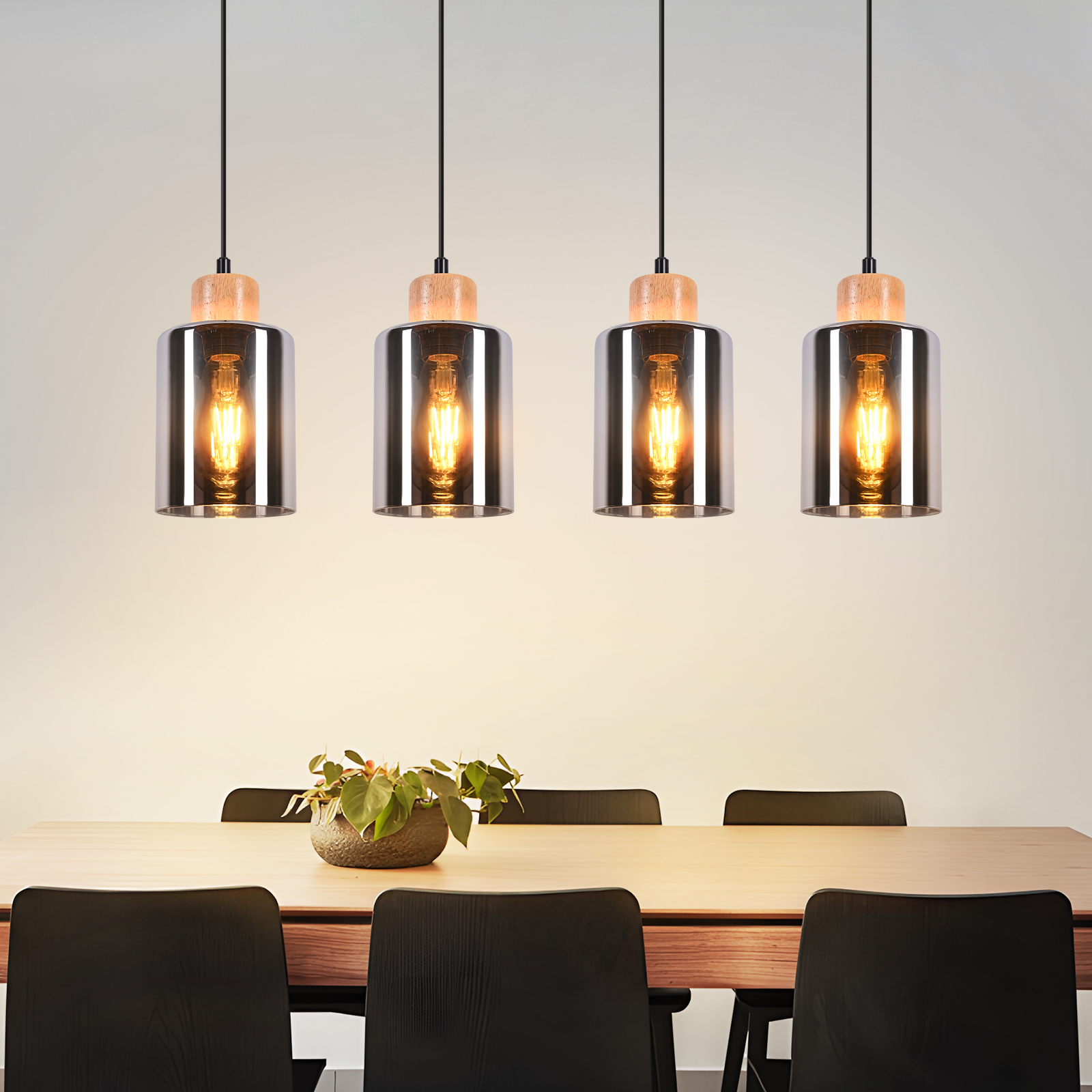 Cuatro lámparas colgantes cuelgan sobre una mesa de comedor con un centro de mesa de plantas. Sillas negras rodean la mesa. Iluminación suave.