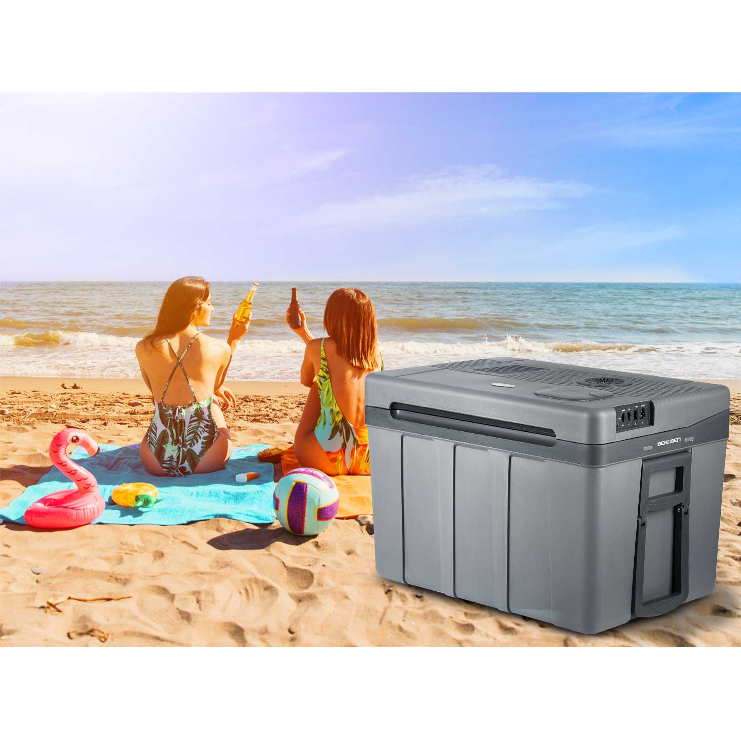 Dwie kobiety na plaży piją piwo, dmuchany flaming, siatkówka, lodówka na piasku, ocean i niebo w tle.